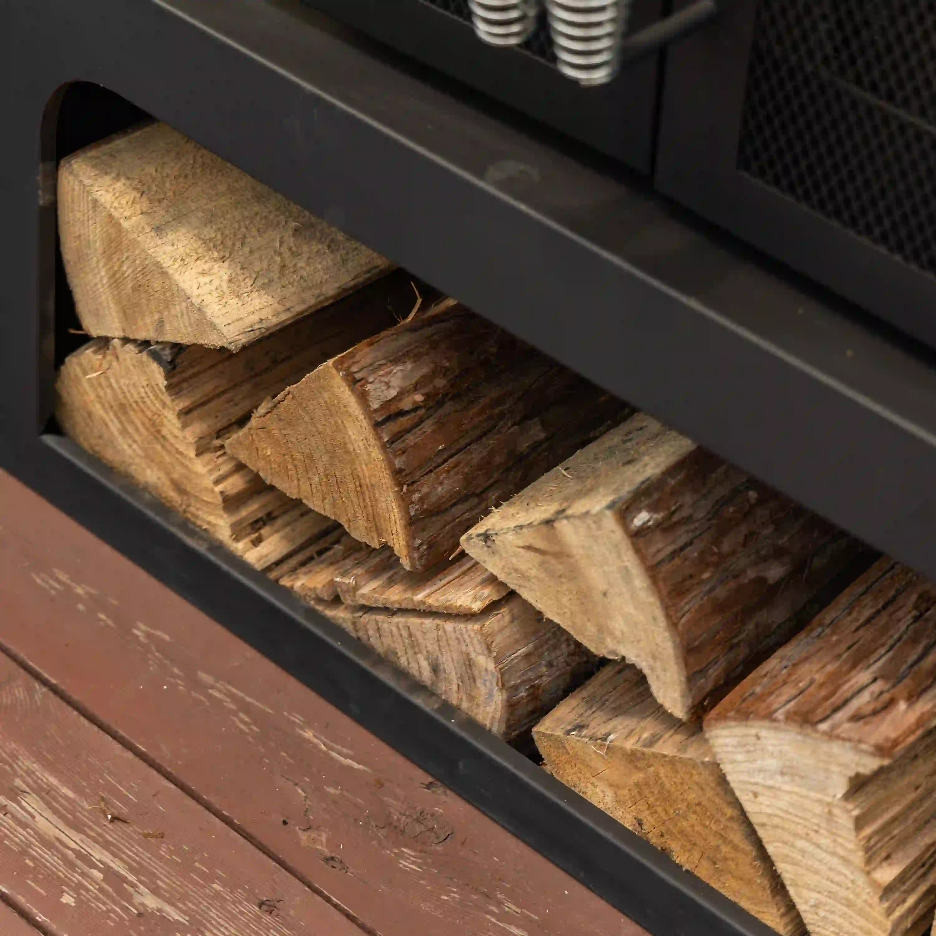 Log storage compartment filled with split firewood inside outdoor fireplace base