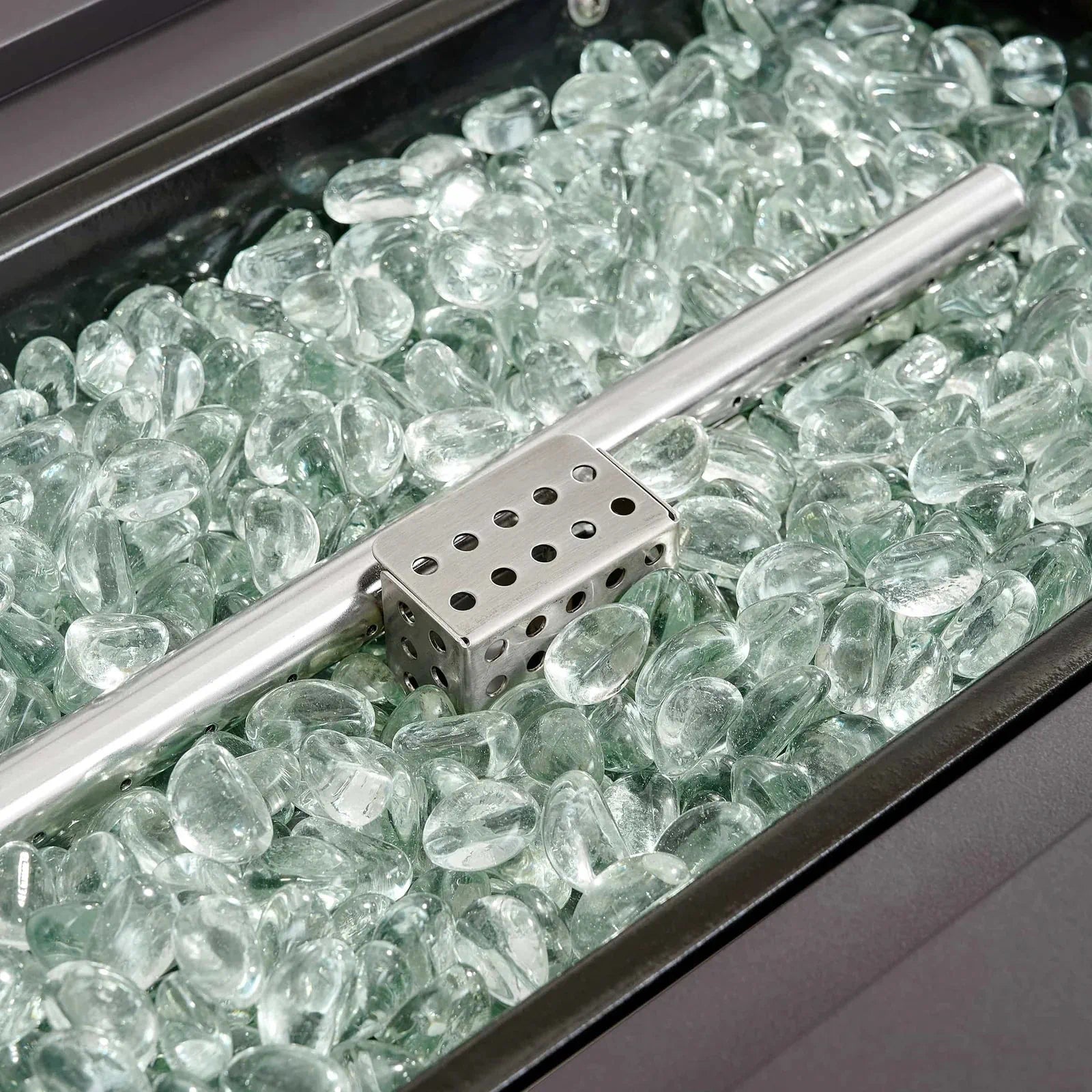 Firepit burner tray with clear blue-tinted glass rocks and perforated metal bar