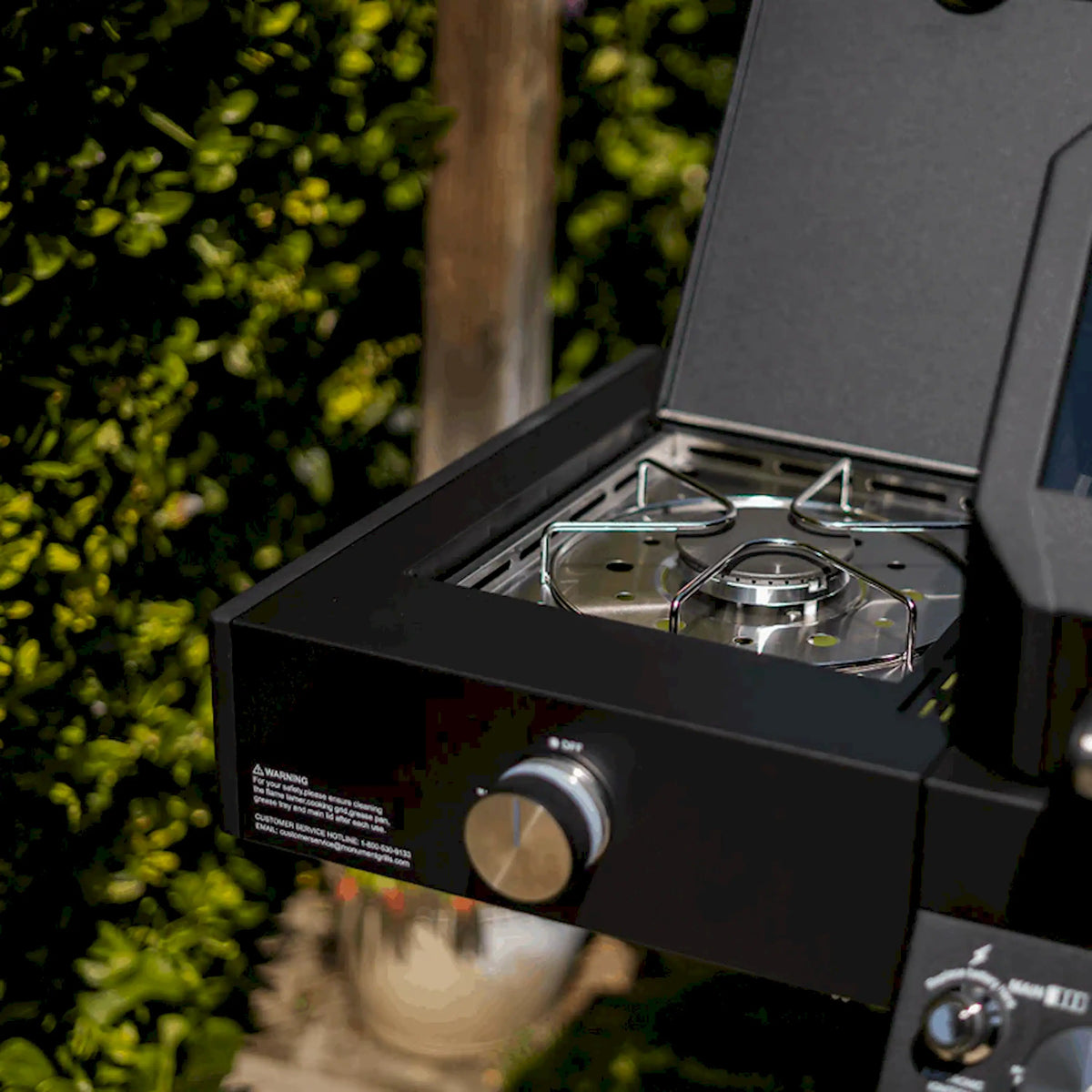 Open side burner compartment with two stainless burners on black grill