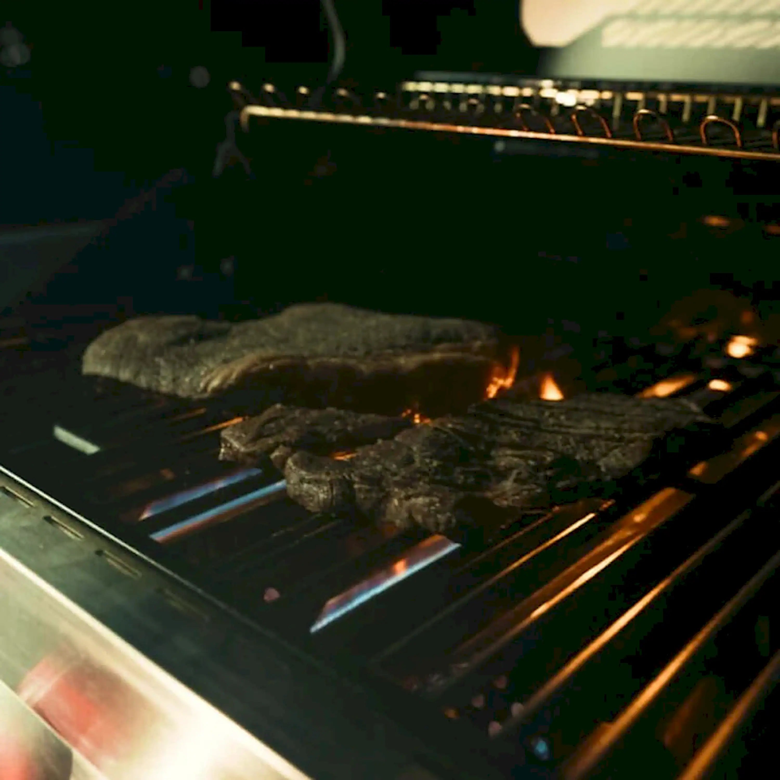 Stainless gas grill with burgers on grates, flames and heat glow