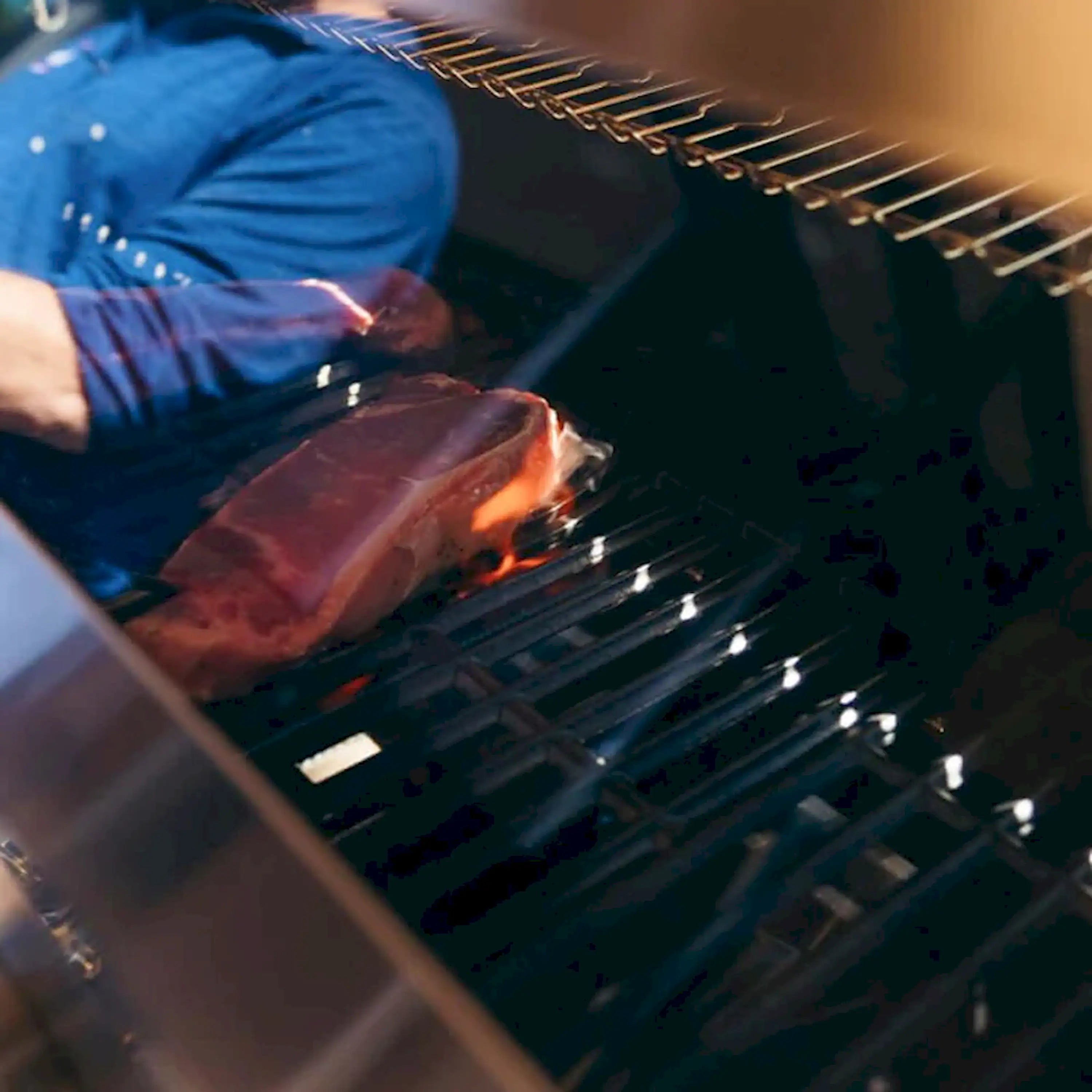 Stainless gas grill with steaks cooking on grates and visible flame