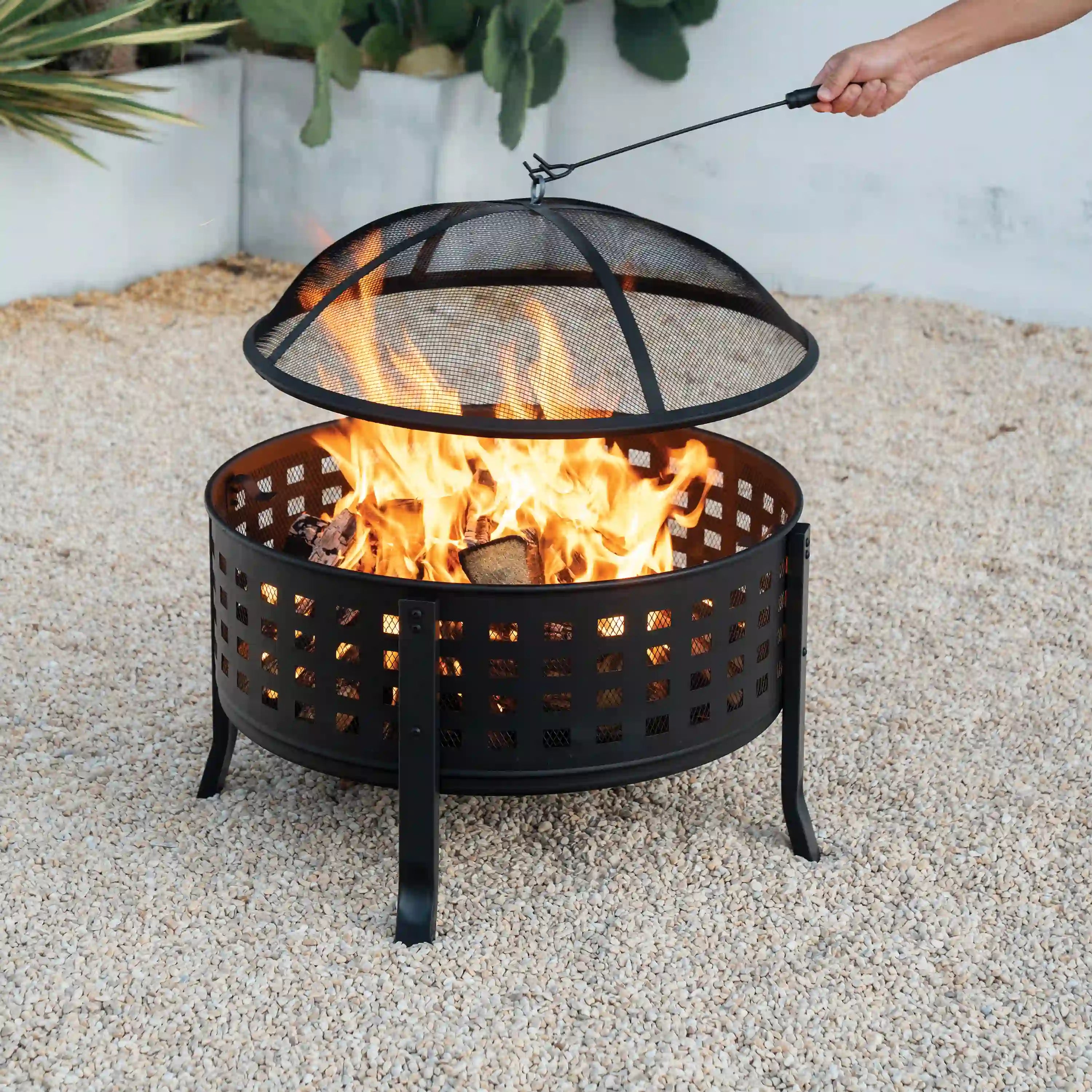 Black round fire pit with flames visible under a mesh spark screen and grill grate