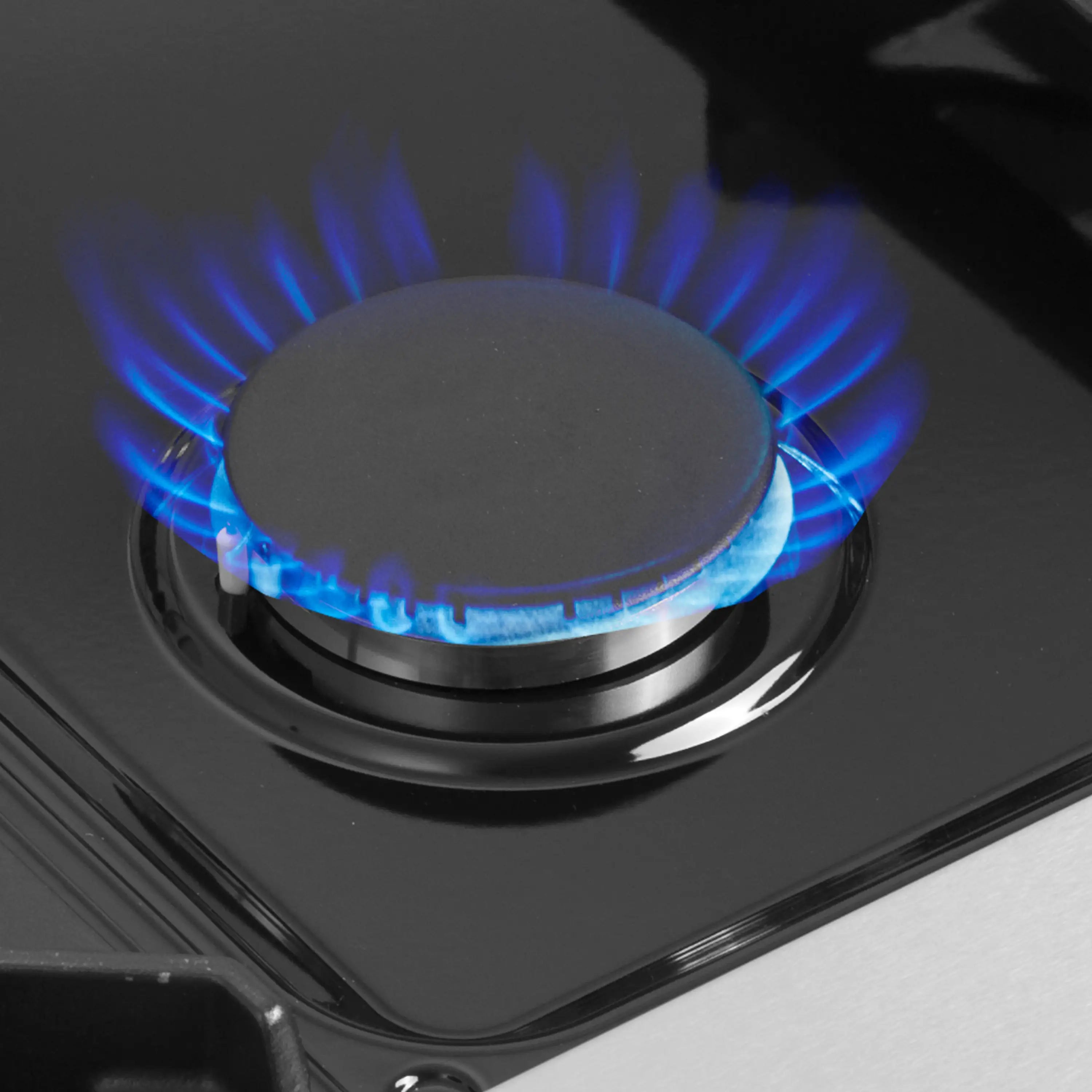 Blue flame burning on a gas range burner head on a dark cooktop