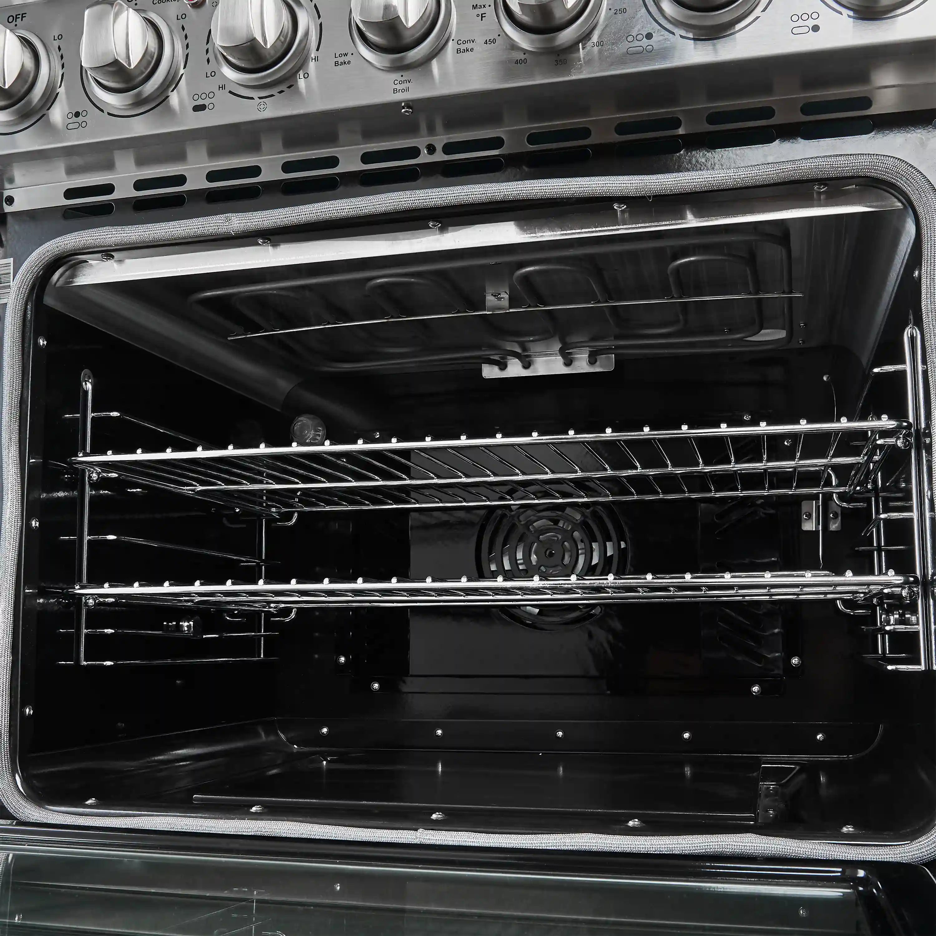 Electric oven interior with wire racks, heating element, and fan at back.