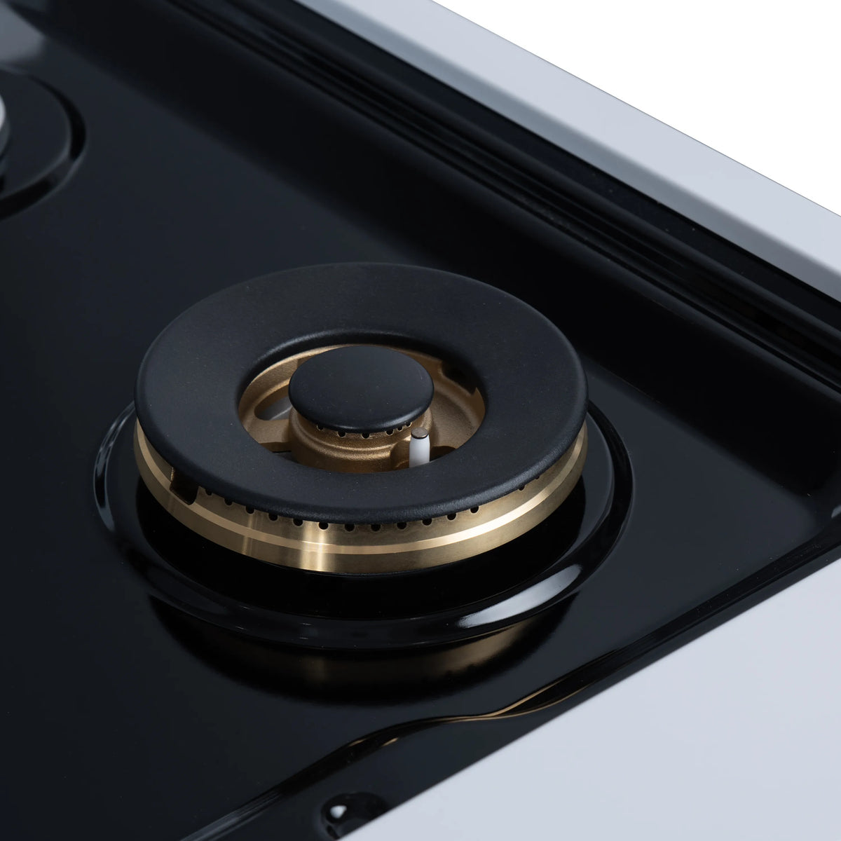 Gas cooktop burner close-up with black cap, brass ring, and dark burner housing