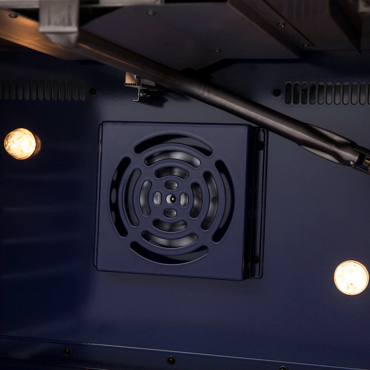 Gas range drawer area with circular fan vent grille and warm oven light glow