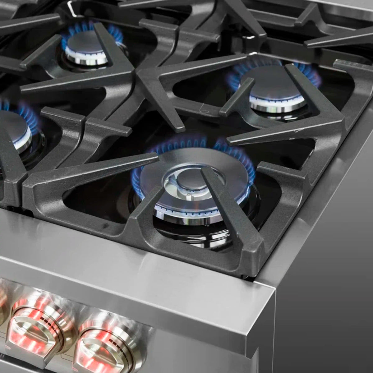 Stainless steel cooktop with black grates and four blue-lit gas burners