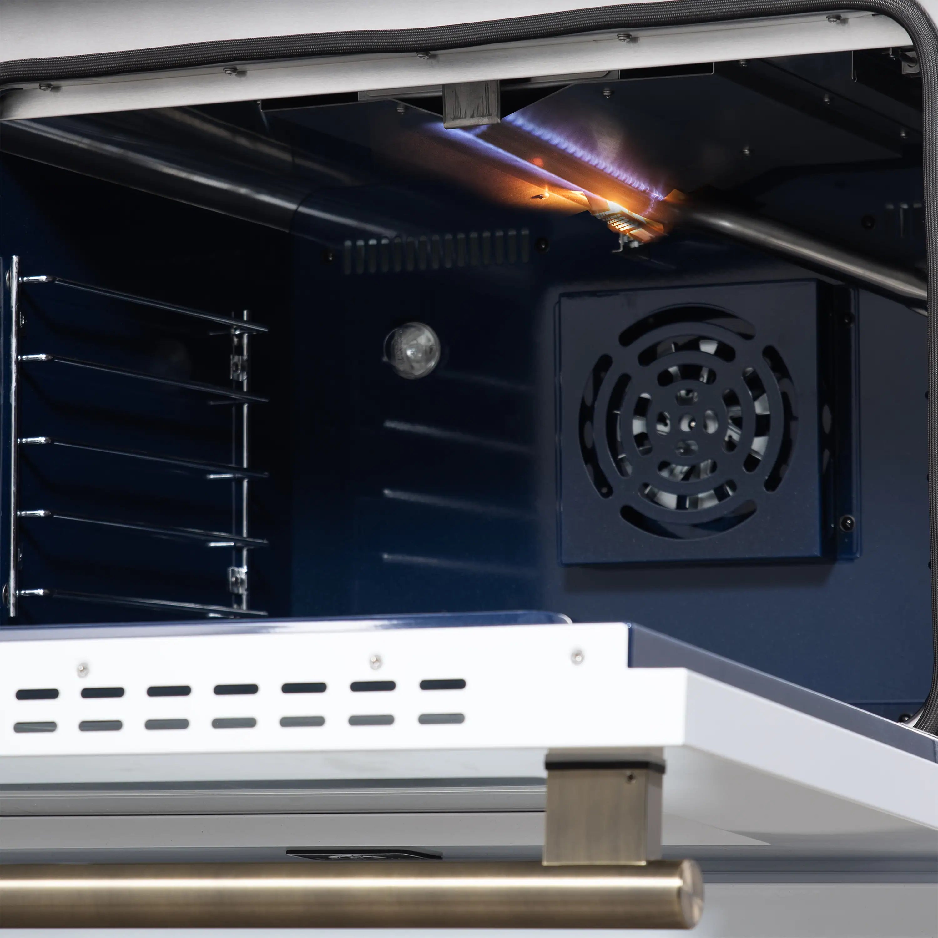 Open convection oven with glowing burner and rear fan vent, viewed inside a gas range