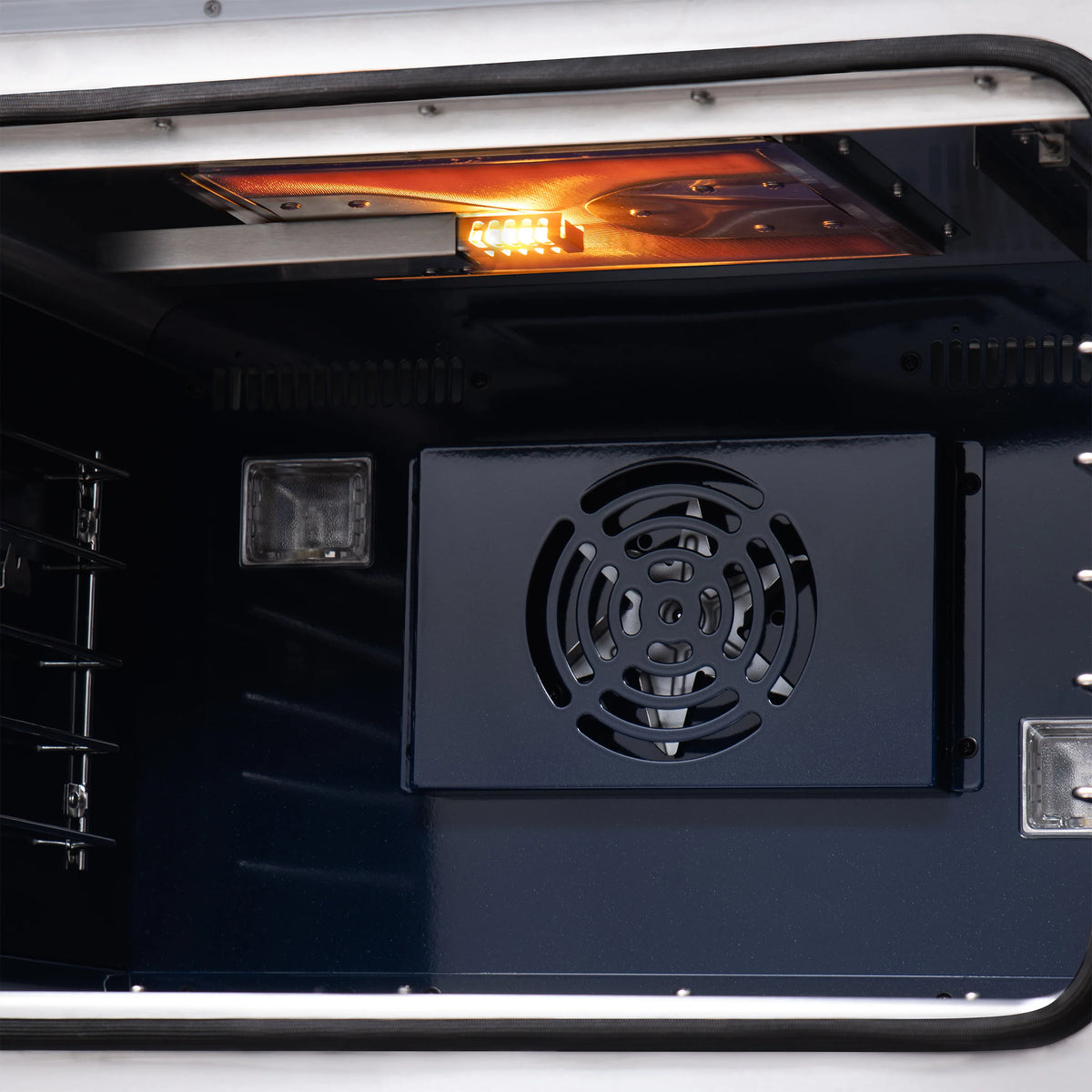 Gas oven interior with rear fan vent and glowing top burner flame