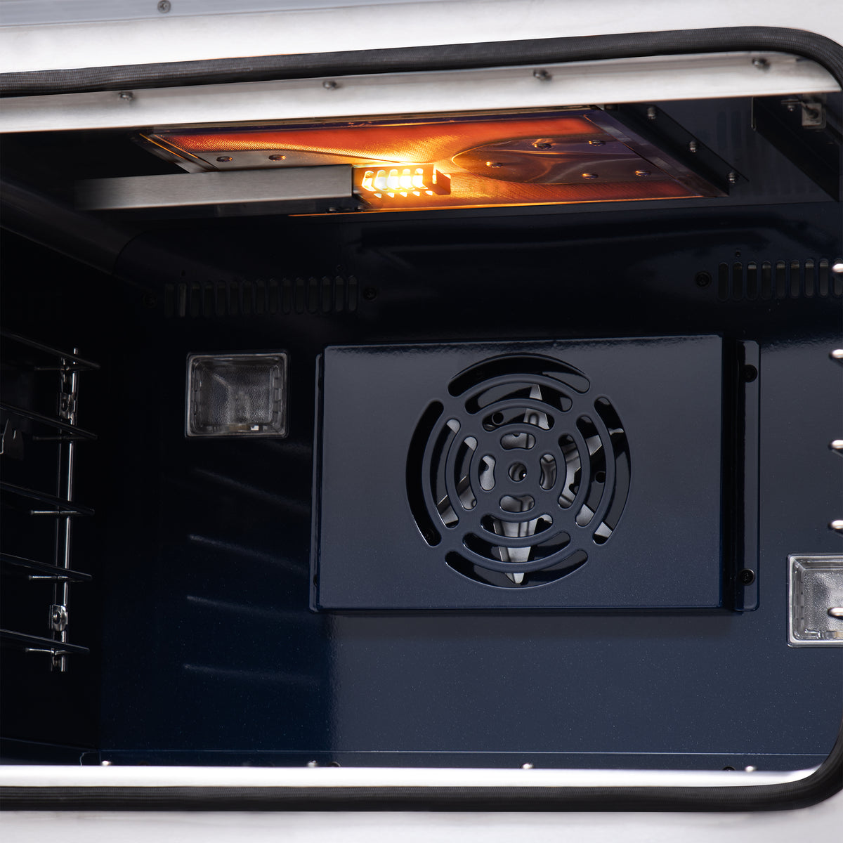 Lit oven interior of black gas range with convection fan vent and wire racks