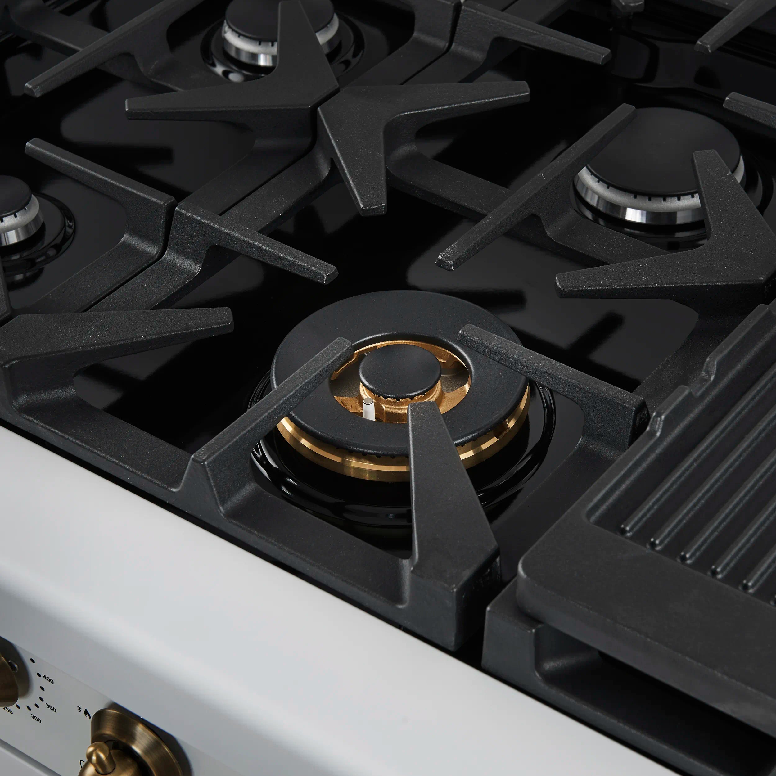 Black gas cooktop grate with gold burner head and white range trim.