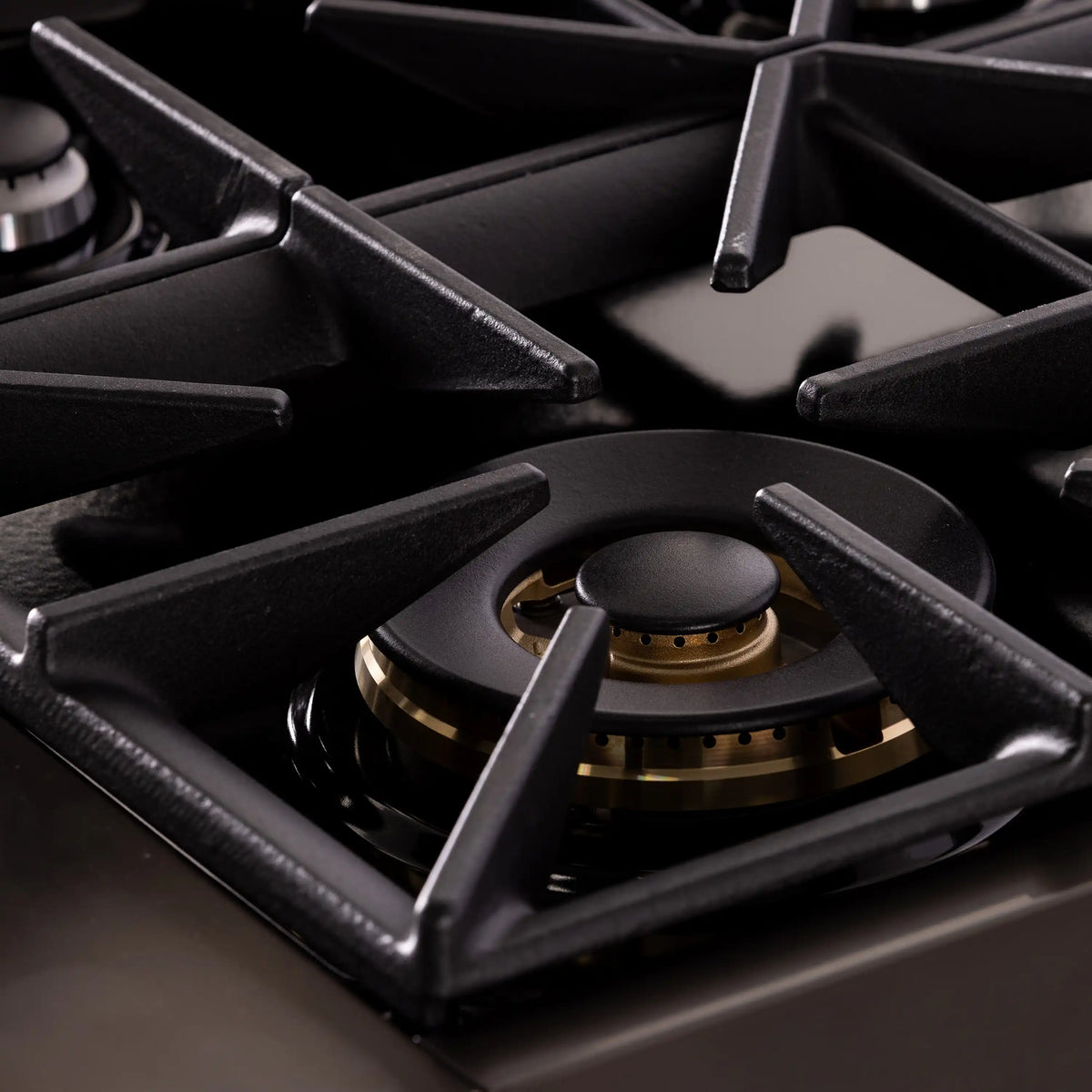 Dark propane cooktop burner head with gold ring and black cast-iron grates