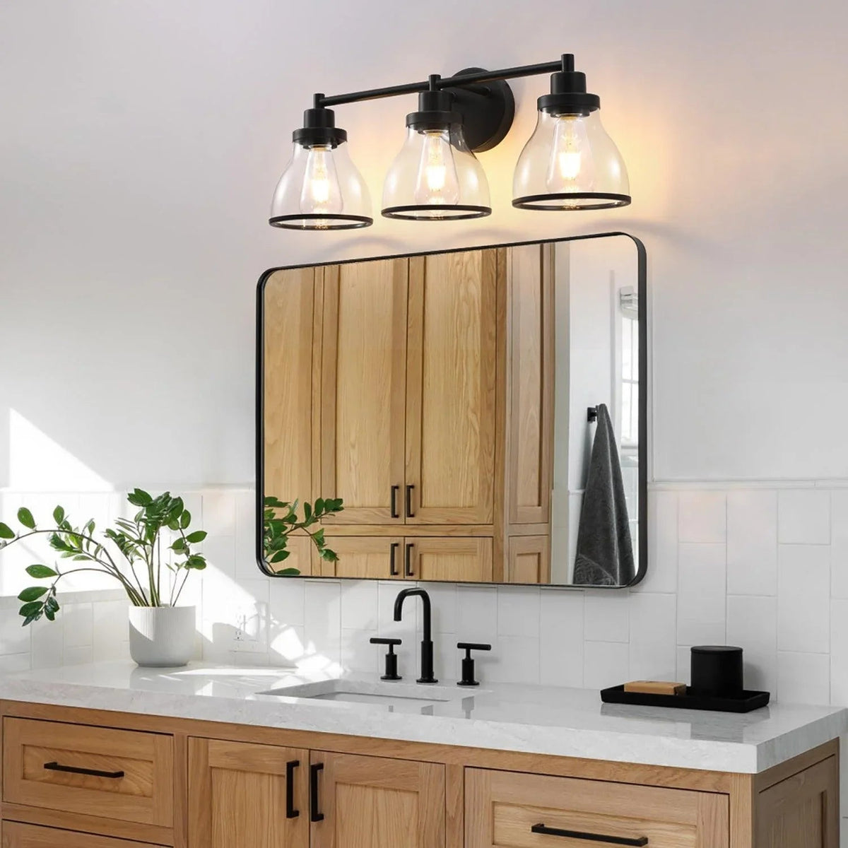 Black 3-light bathroom vanity light with clear glass shades above a mirror
