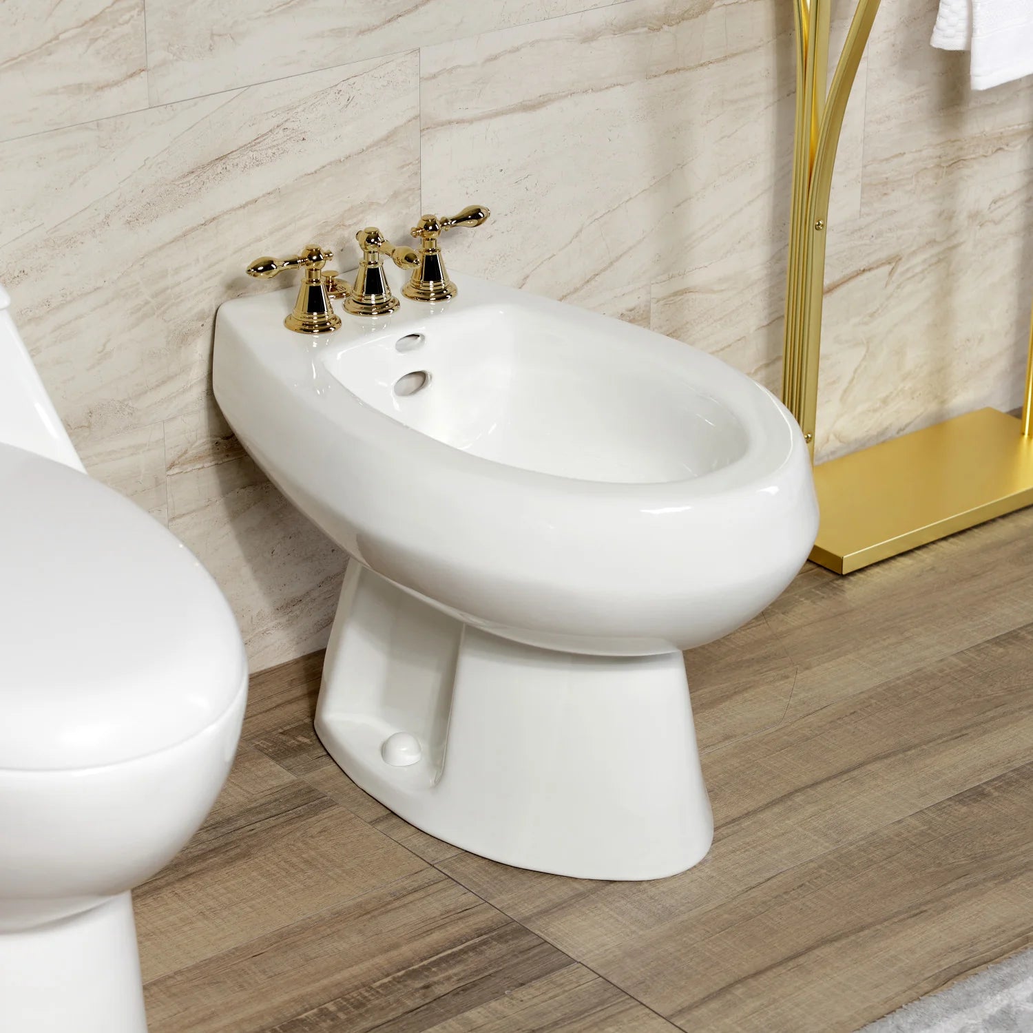 Polished brass three-handle bidet faucet with pop-up on a white toilet area