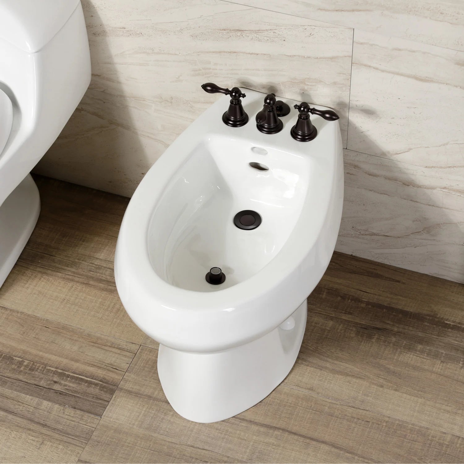 Three-handle oil-rubbed bronze bidet faucet on a white bidet with metal drain opening