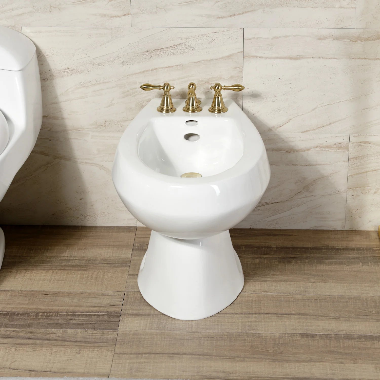 Three-handle brushed brass bidet faucet with pop-up on white pedestal bidet
