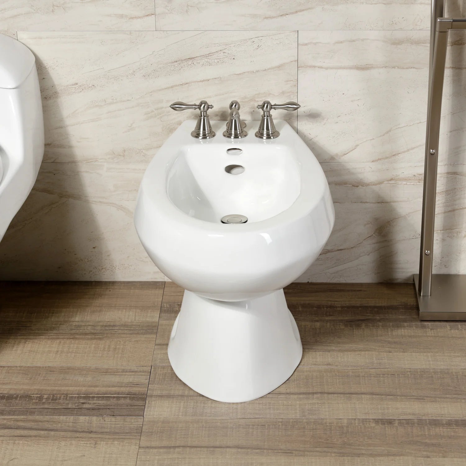 White pedestal bidet with brushed nickel three-handle faucet set.