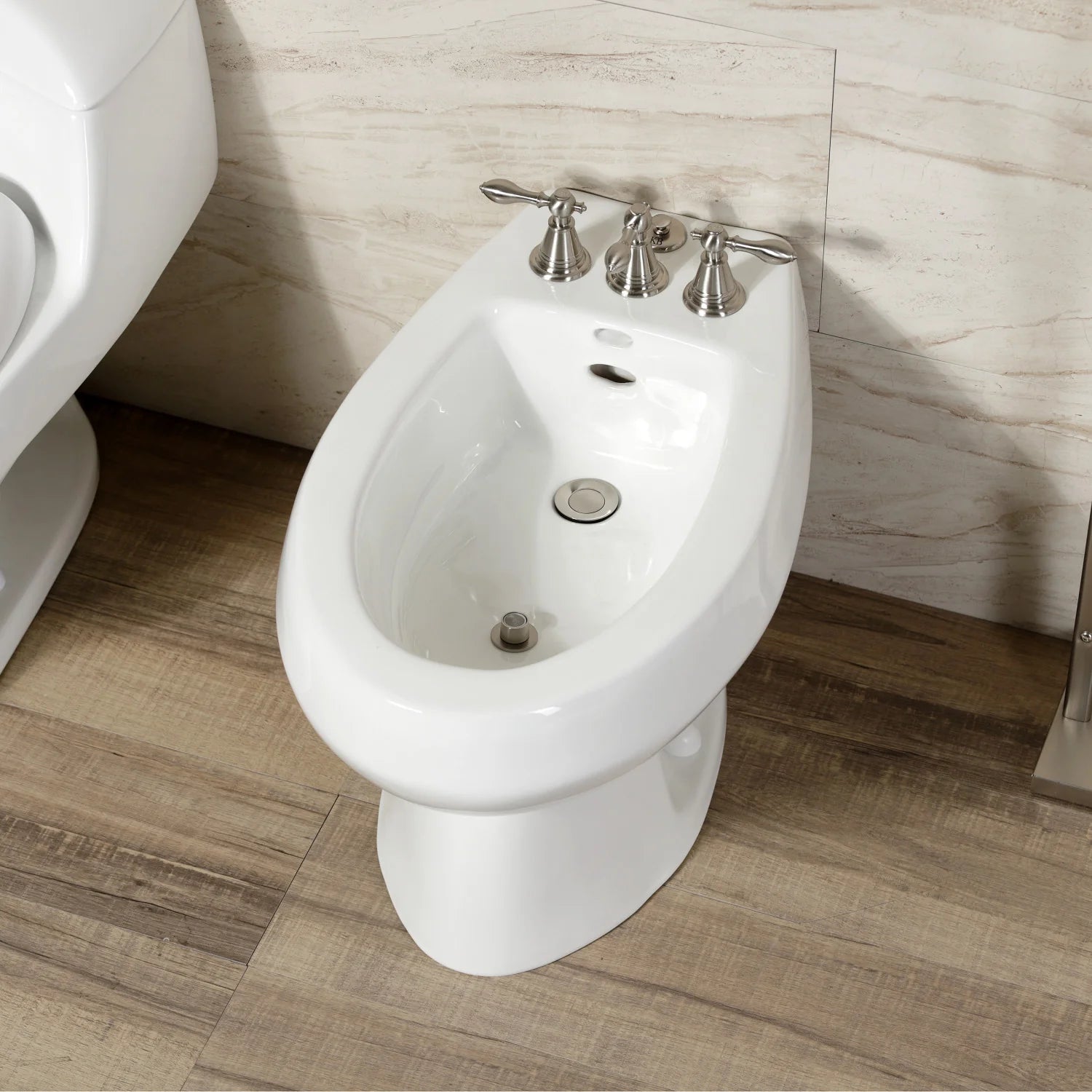 White bidet with brushed nickel three-handle faucet and metal pop-up controls.