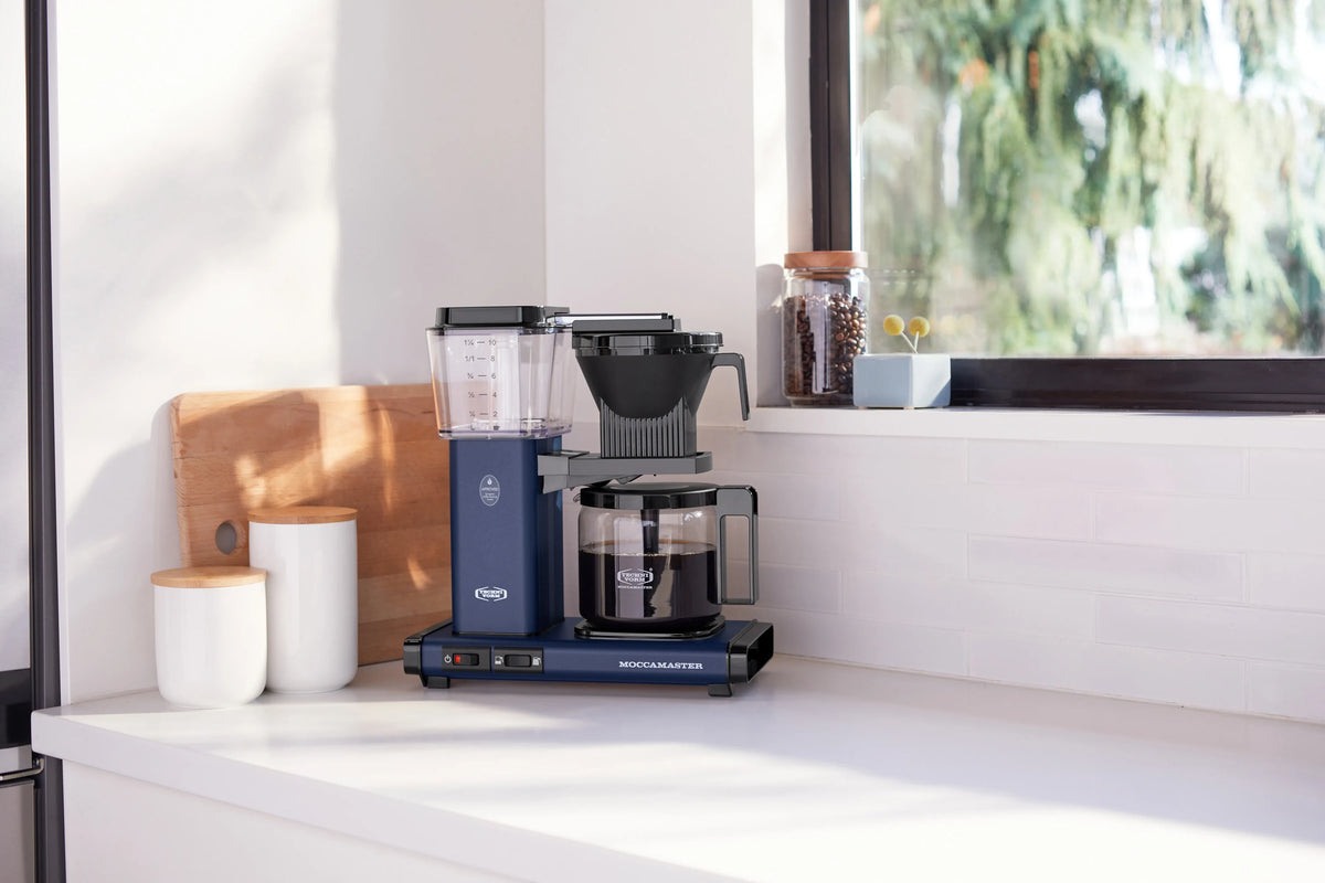 Midnight blue coffee maker with glass carafe and clear water reservoir beside it