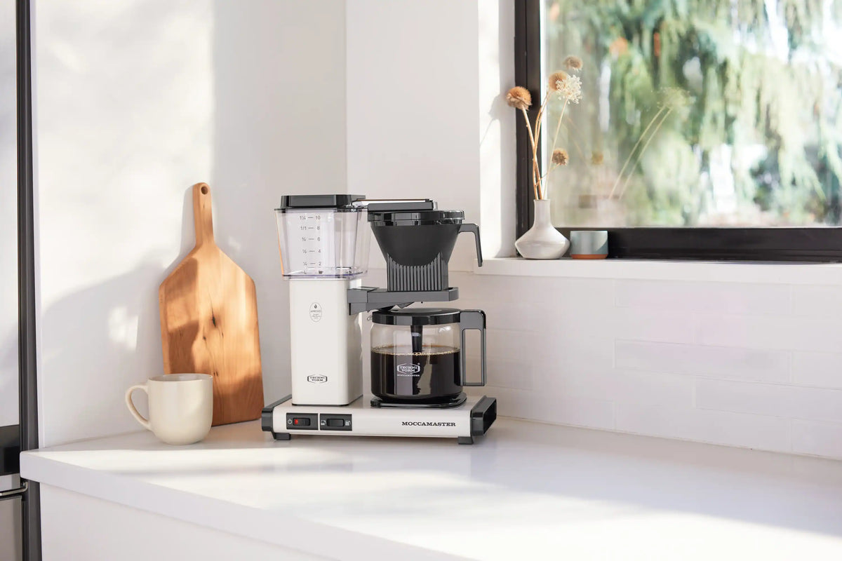 Moccamaster 10-cup coffee maker in off-white with glass carafe on countertop, side angle