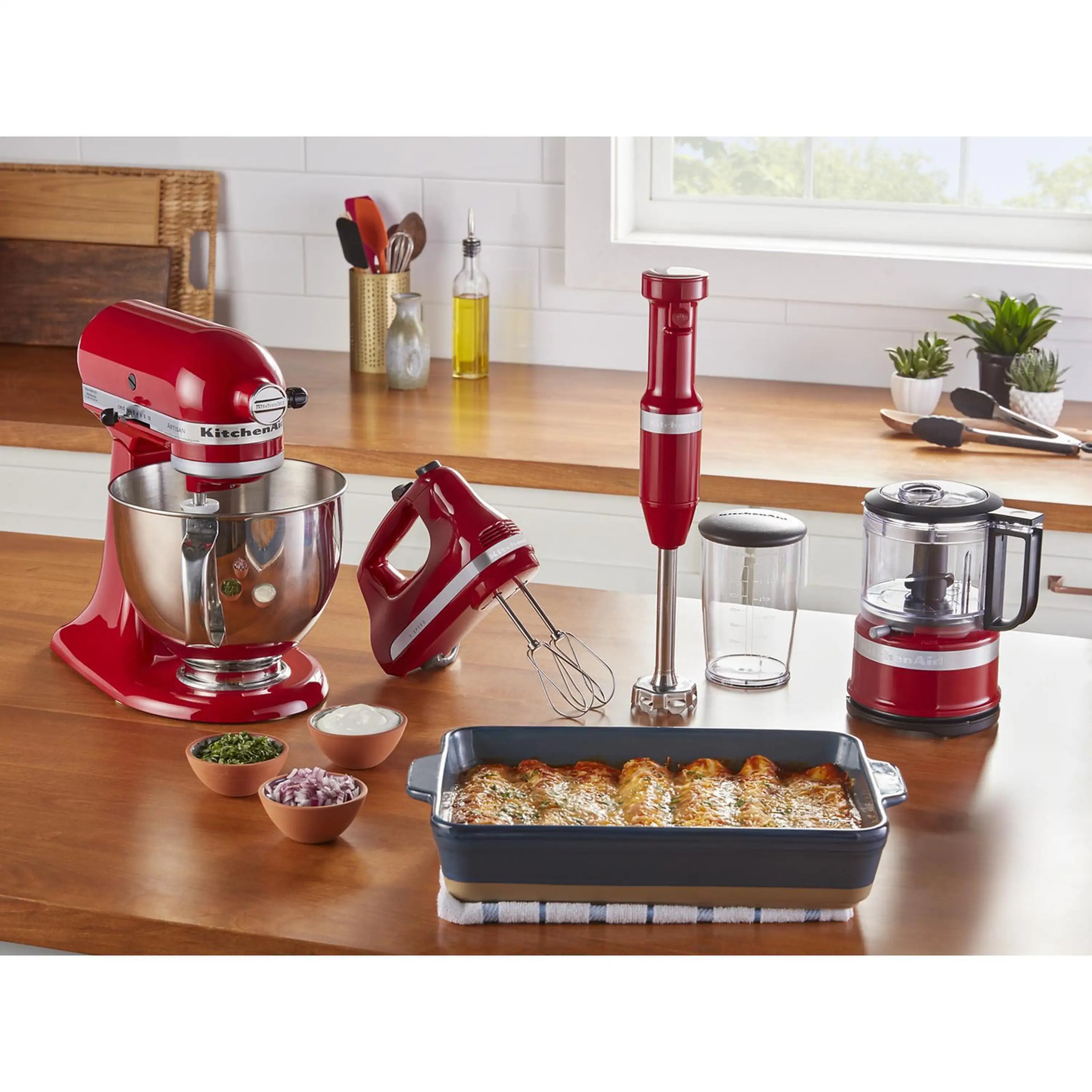 Red KitchenAid hand mixer on kitchen counter with beaters and mixing accessories