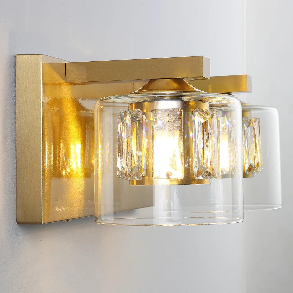 Two-light bathroom vanity light with clear glass cylinder shades and golden metal backplate
