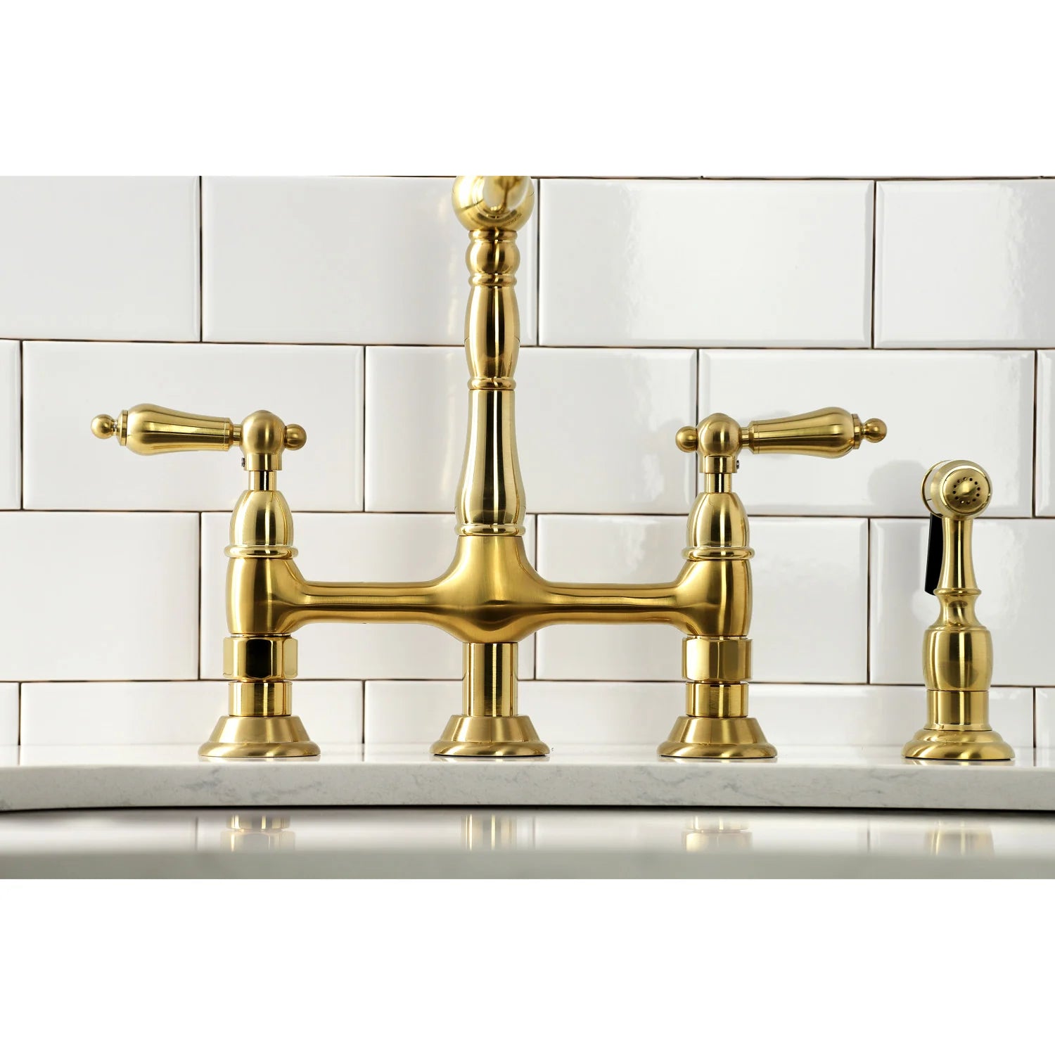 Brushed brass bridge faucet with three handles and side sprayer on countertop