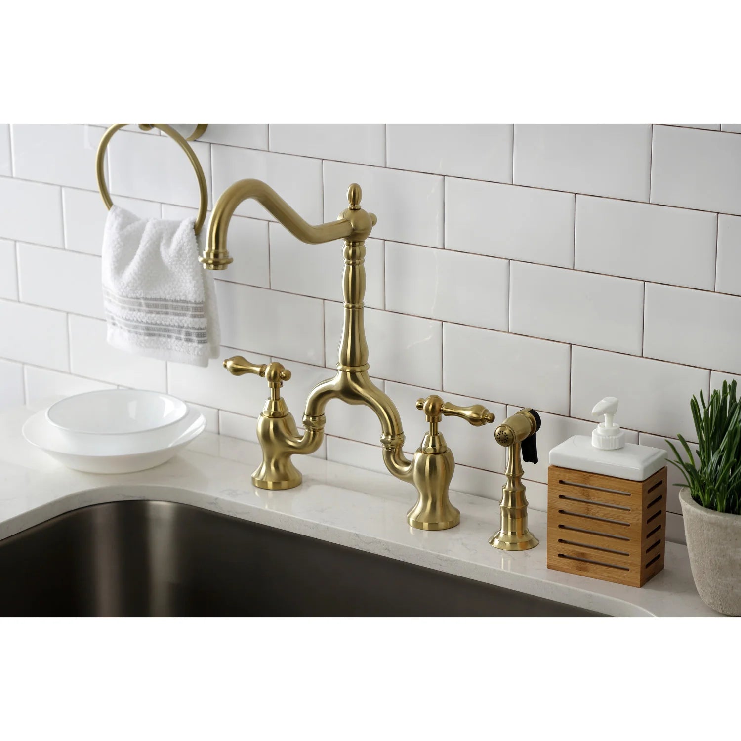 Brushed brass bridge faucet with side sprayer and two cross handles on sink
