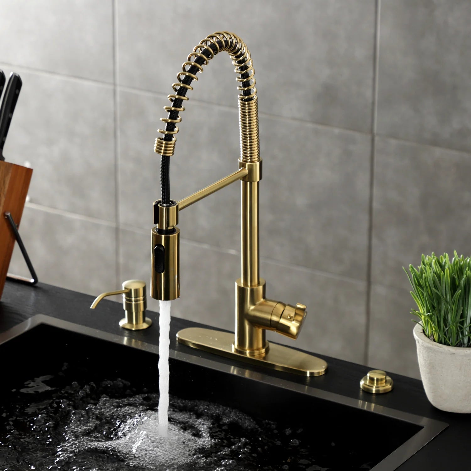 Brushed brass deck-mount kitchen faucet with coiled sprayer and water flowing