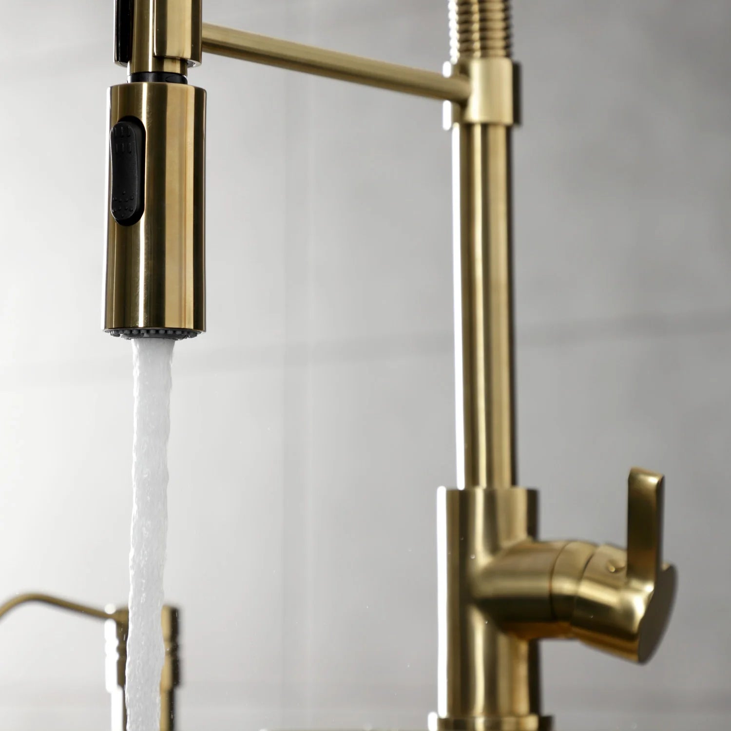 Brushed brass single-handle kitchen faucet with spray head delivering water stream