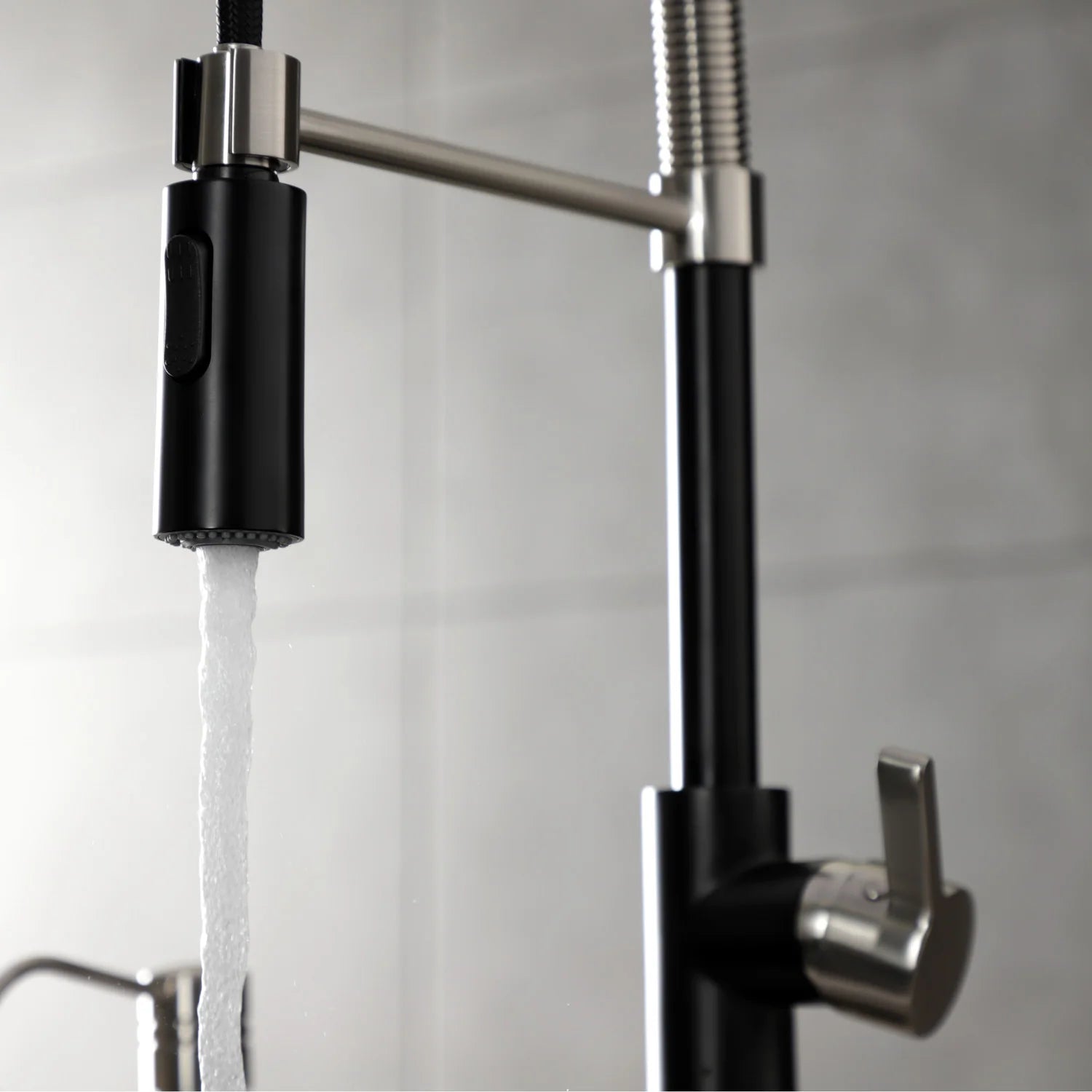 Close-up of matte black pre-rinse faucet handle and flexible hose with water flow