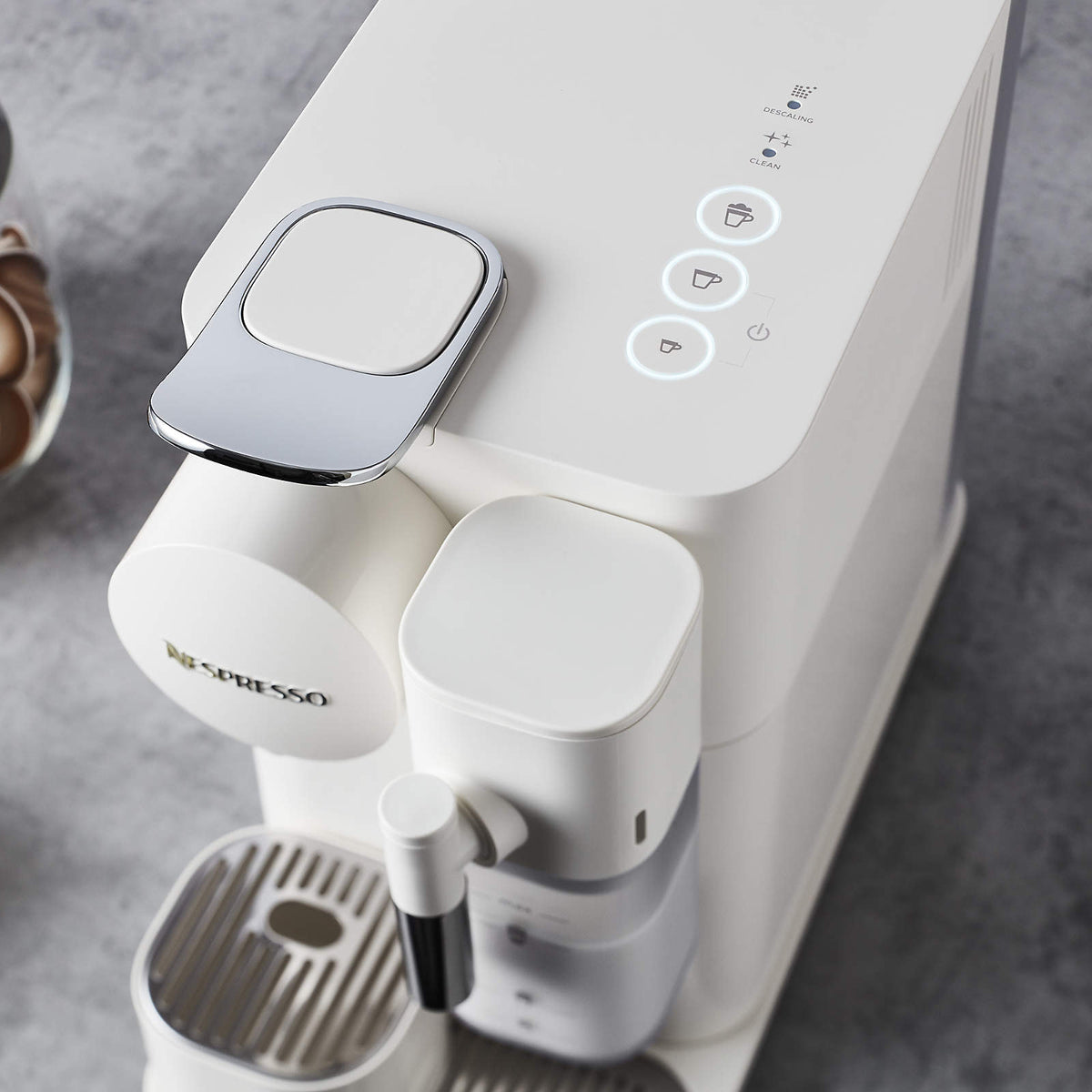 White machine close-up showing frother spout, cup stand, and control icons