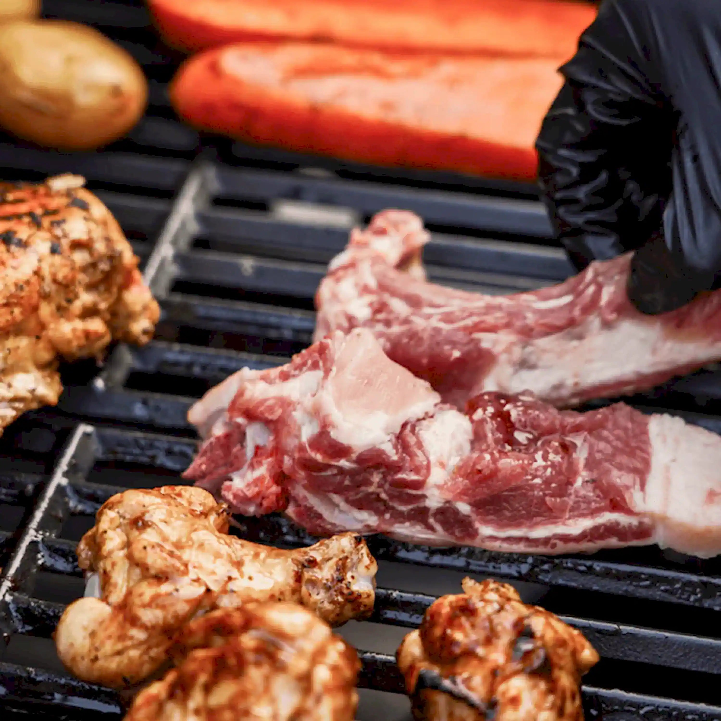 Two-burner propane gas grill grates with sizzling bacon, chicken, and sausage