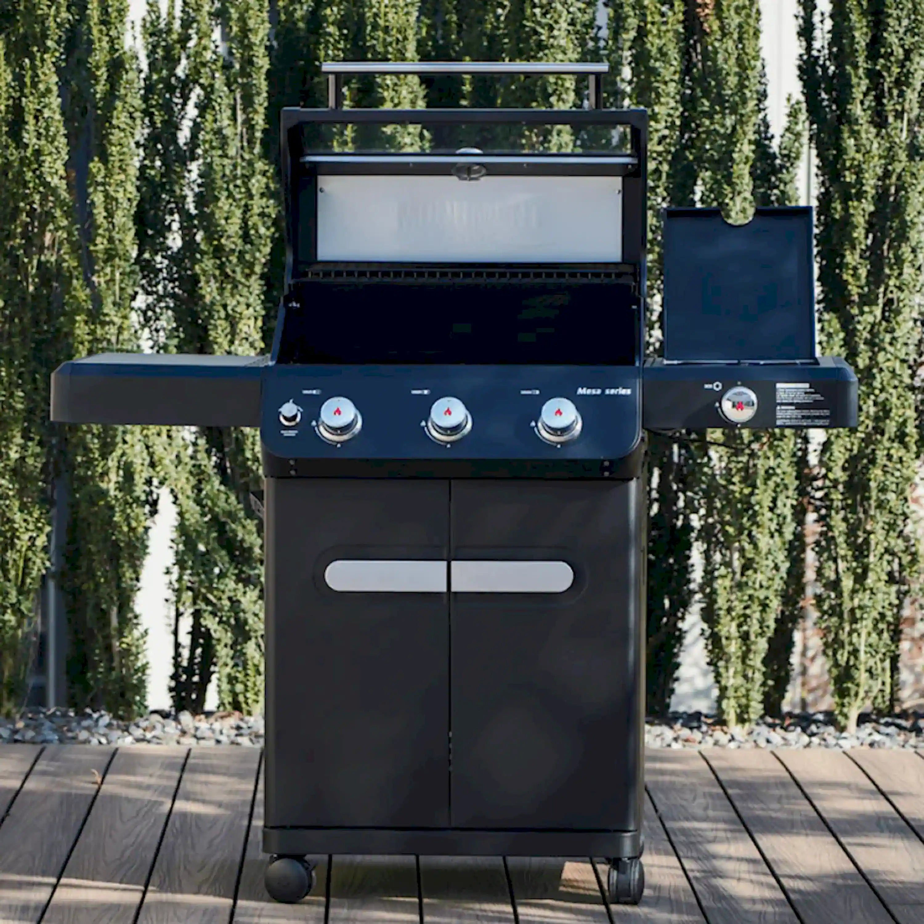 Black propane grill standing outdoors, three burner control knobs and front panels visible