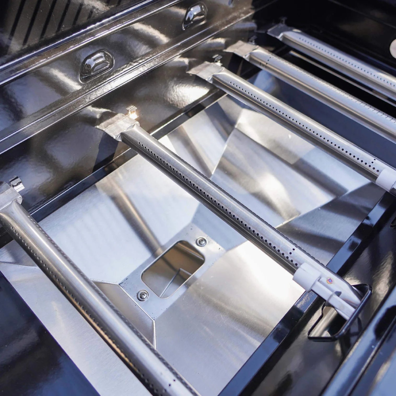 Open stainless steel grill interior with heat shield panels and dual burner rails