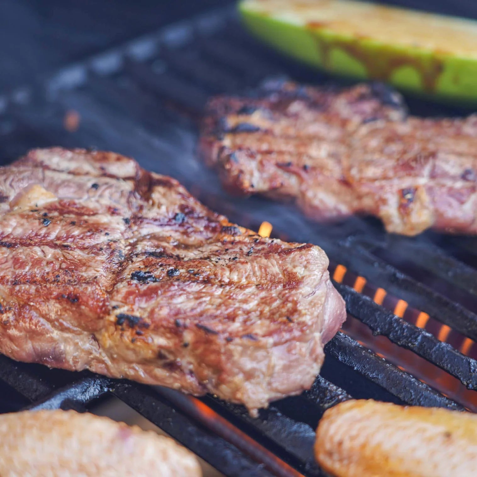Grilled meat on dark stainless steel grill grates with visible char and smoke