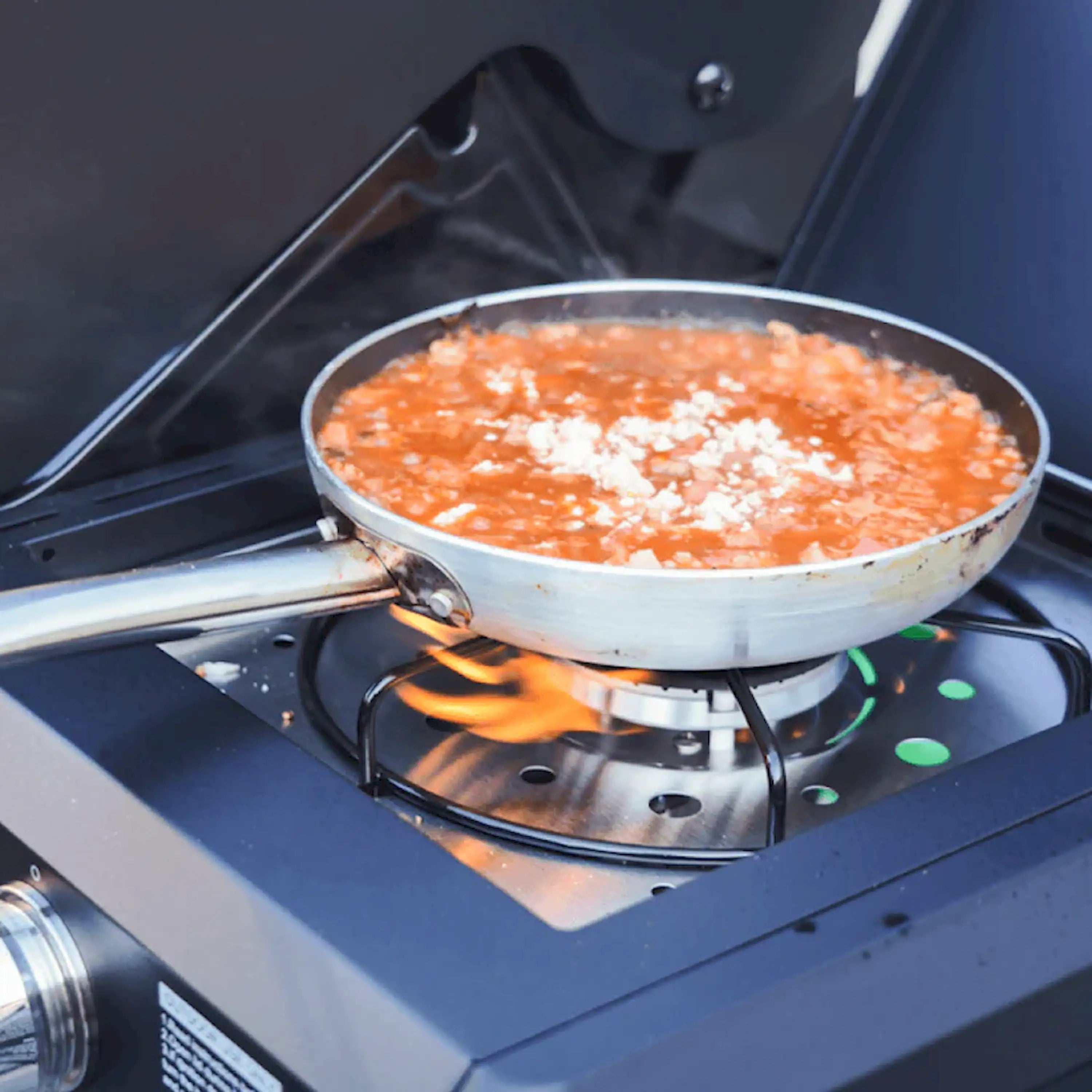 Gas grill burner with flames under a metal skillet on the cooking surface