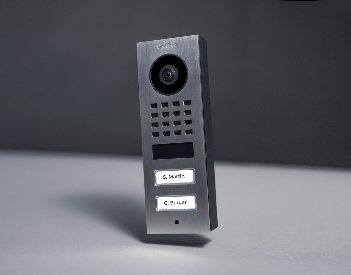 Brushed silver DoorBird surface-mount IP video door station with camera lens and call name buttons