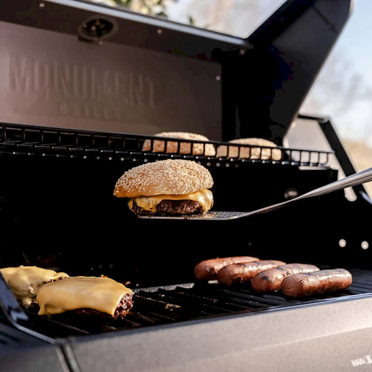 Open black gas grill cooking grate with burger and sausages