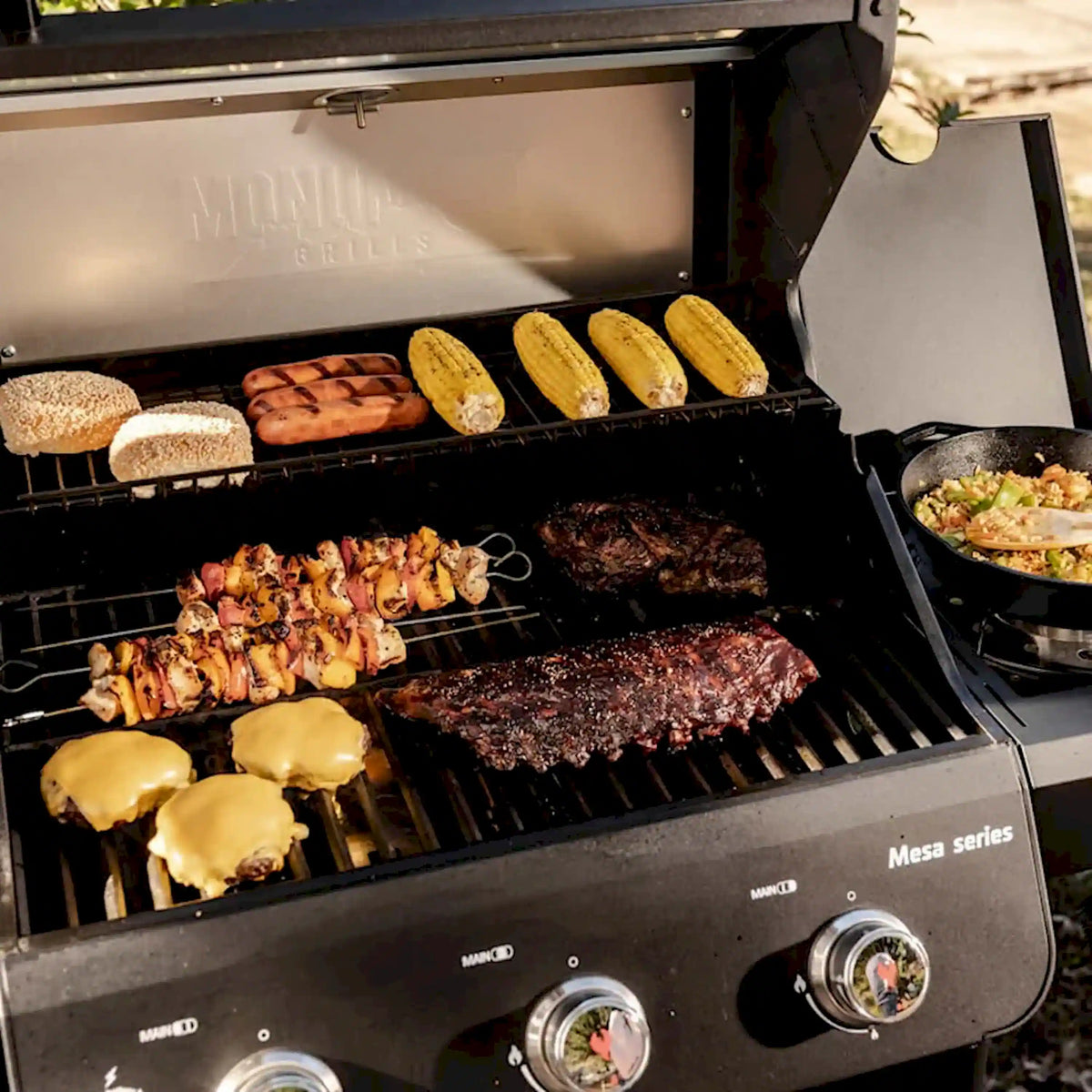 Black propane grill with lid open, corn, buns, chicken skewers, and burgers on grates