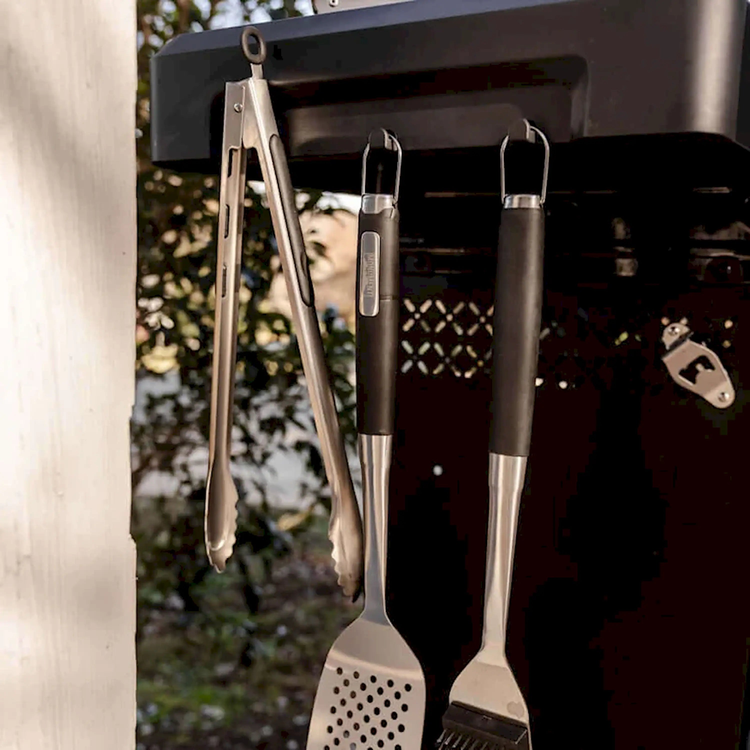 Black propane grill with two utensil tools hanging from the open lid