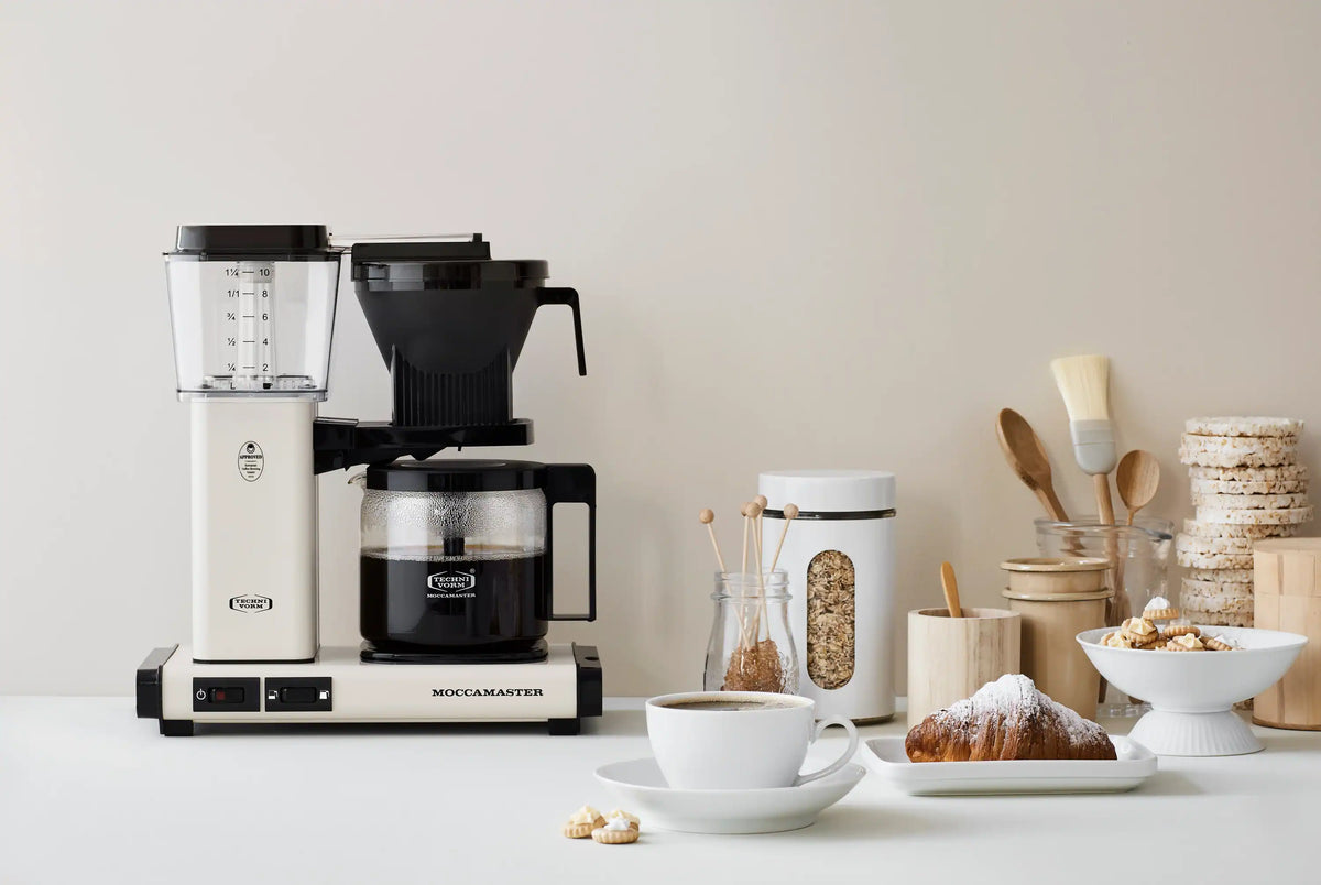 Moccamaster 10-cup coffee maker in off-white with glass carafe and black filter holder, side view