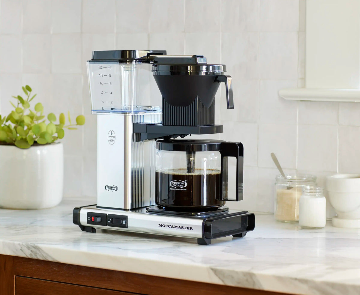 Moccamaster coffee maker with glass carafe and black brew basket on polished base.