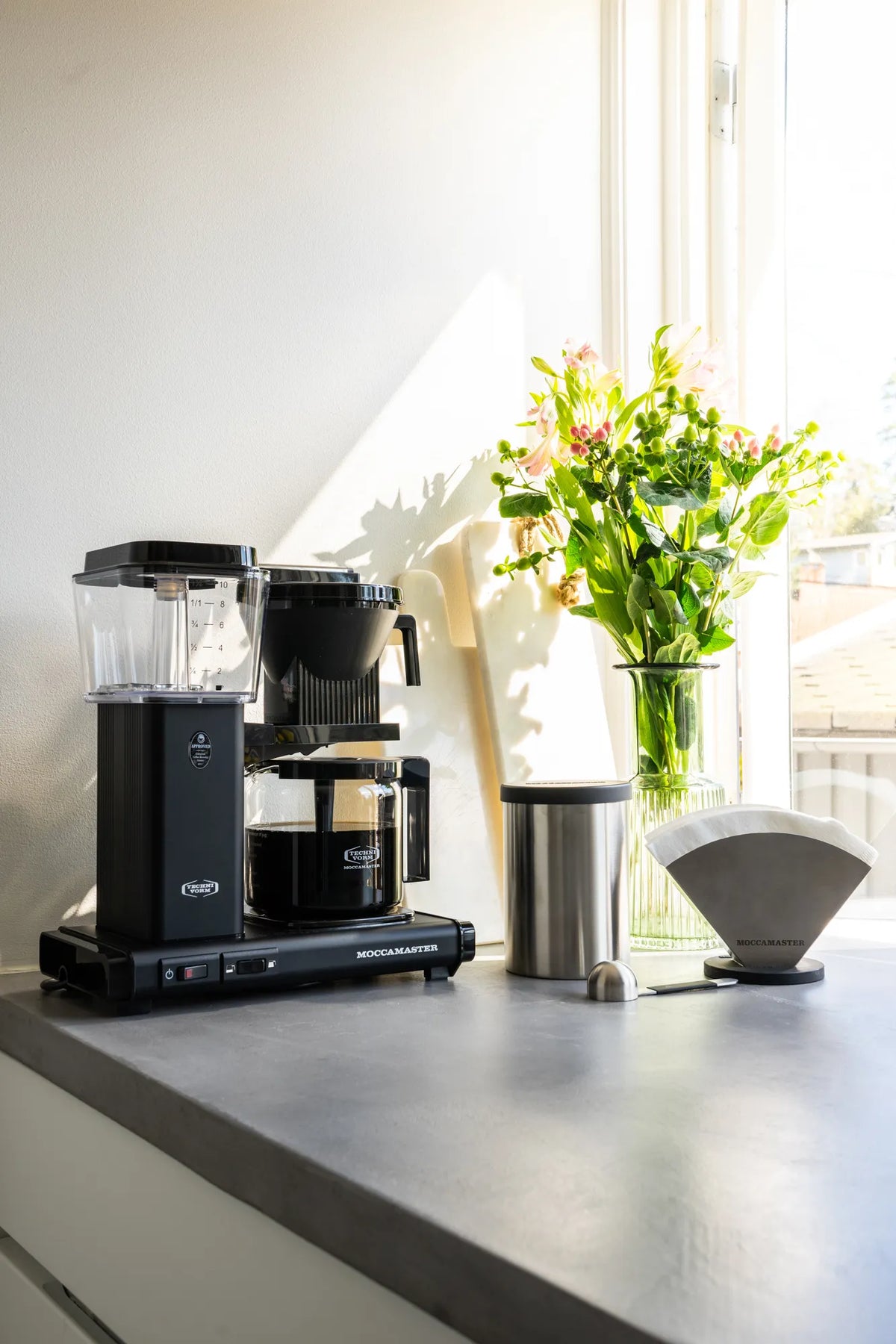 Moccamaster matte black coffee maker with glass carafe and filter tank on countertop
