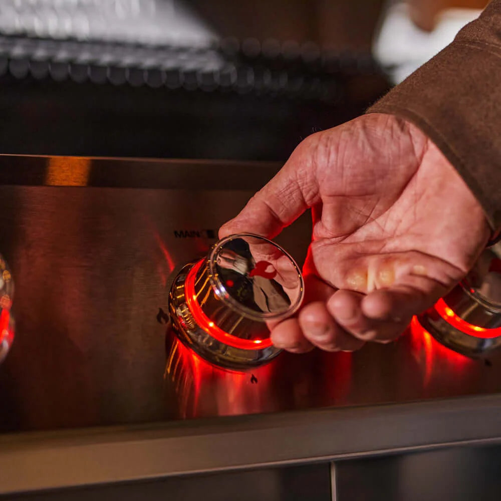 Stainless steel grill with control knob near ignition, red flame visible under open lid