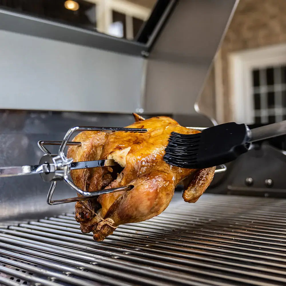 Rotisserie-style chicken roasting on grill grates with basting brush