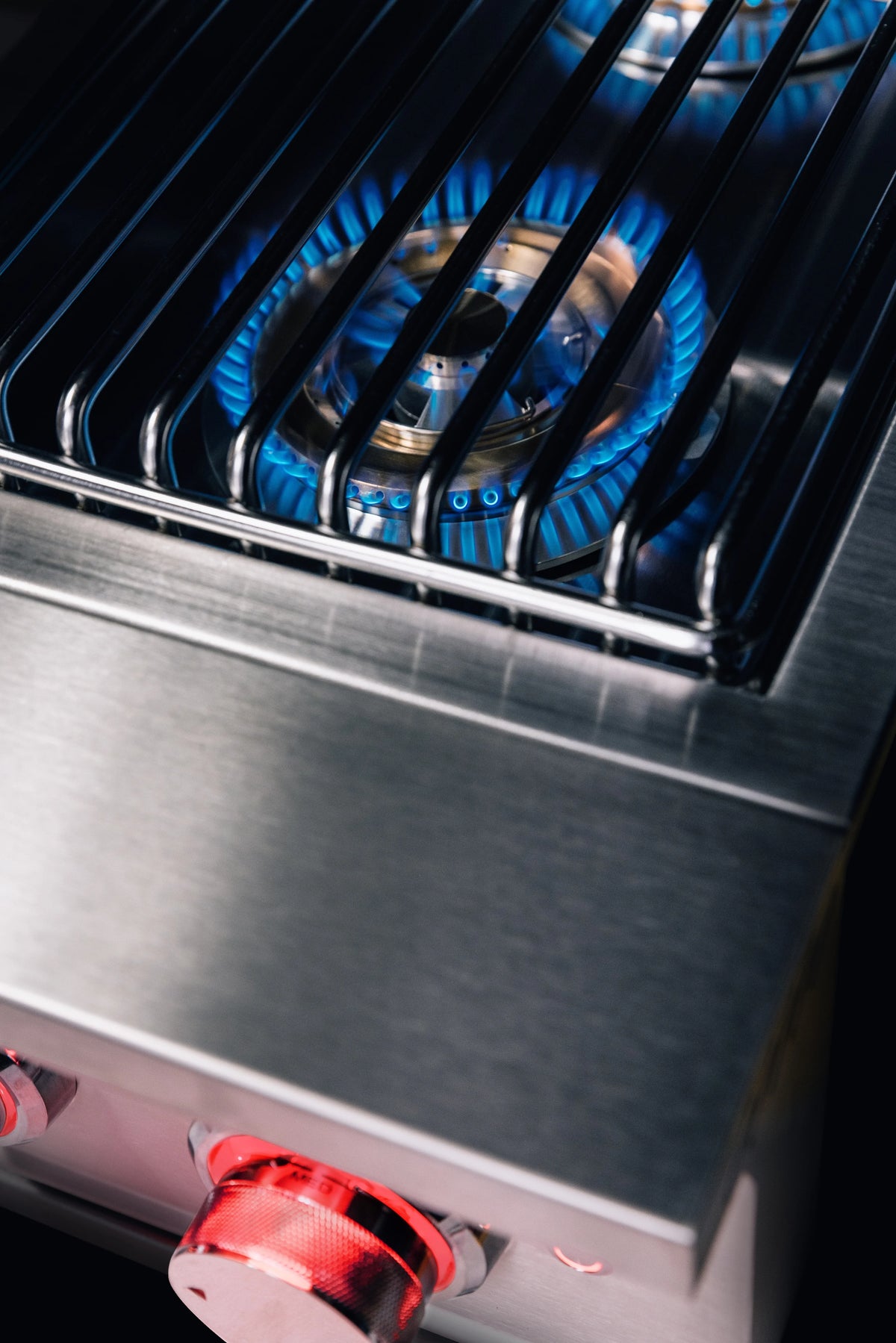 Natural gas side burner grate with bright blue flames and stainless front panel