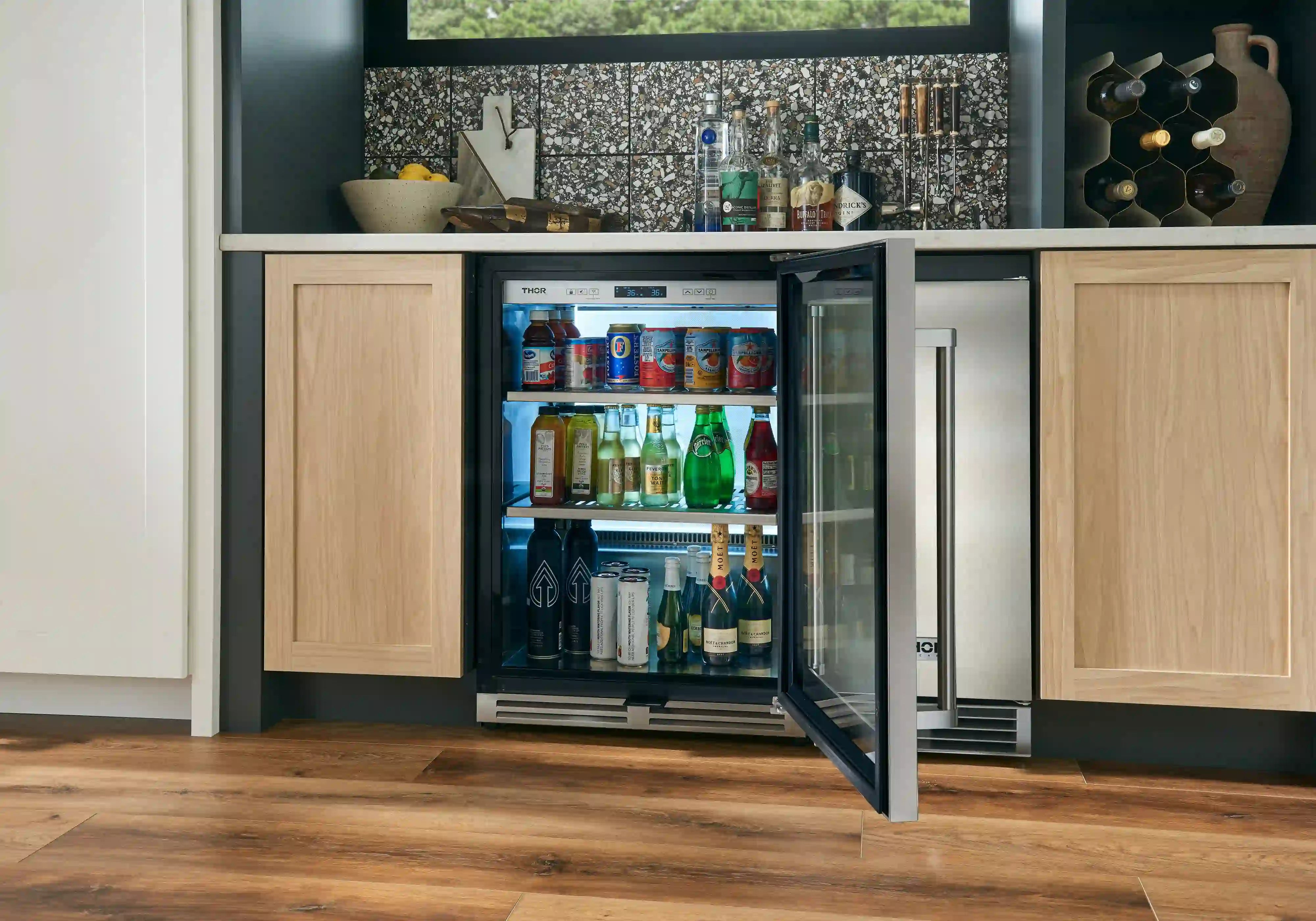 Stainless beverage cooler with open glass door and interior shelves holding bottles