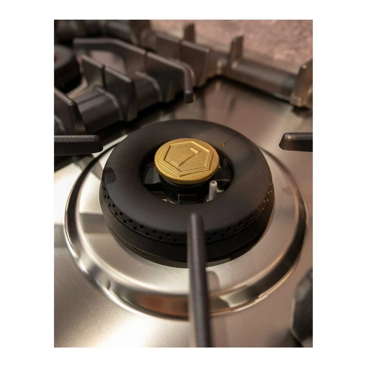 Close-up of brass-cap burner and ring on stainless steel gas cooktop with black grates