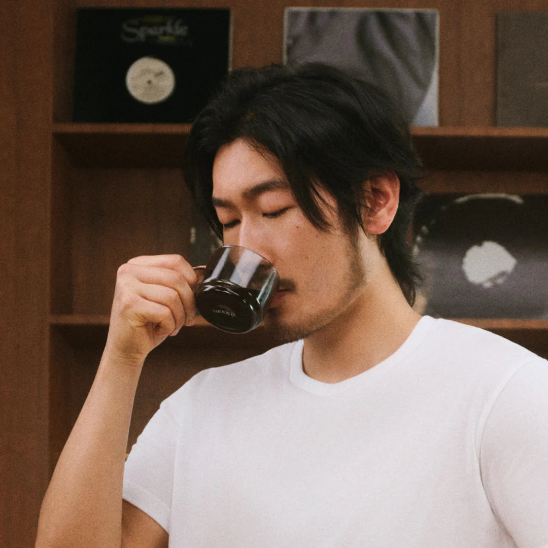 Tasting cup with black handle, person sipping from dark glass mug